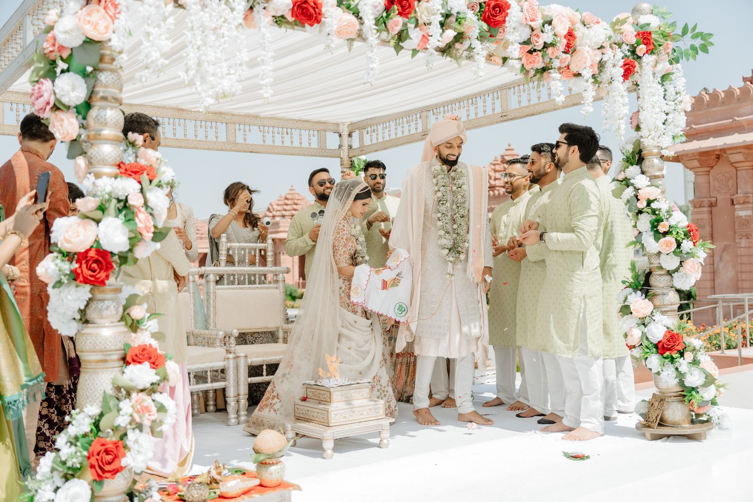 Wedding ceremony setup with red and white floral arrangements under an elegant white canopy.