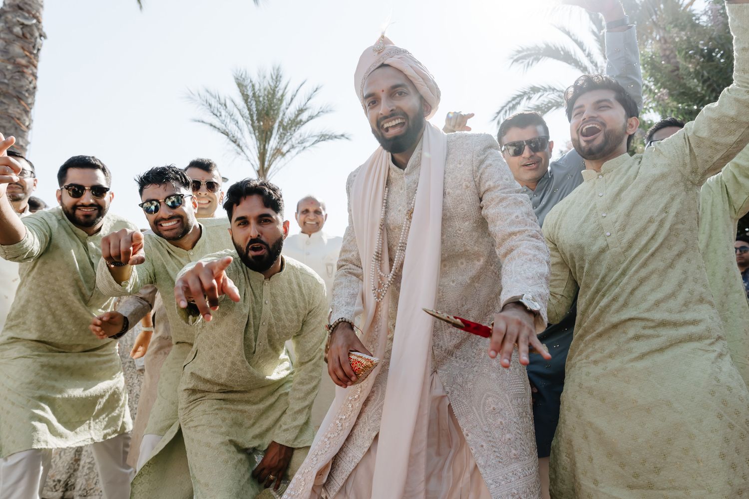 A group wearing traditional light-colored ethnic attire poses together outdoors during a celebration.