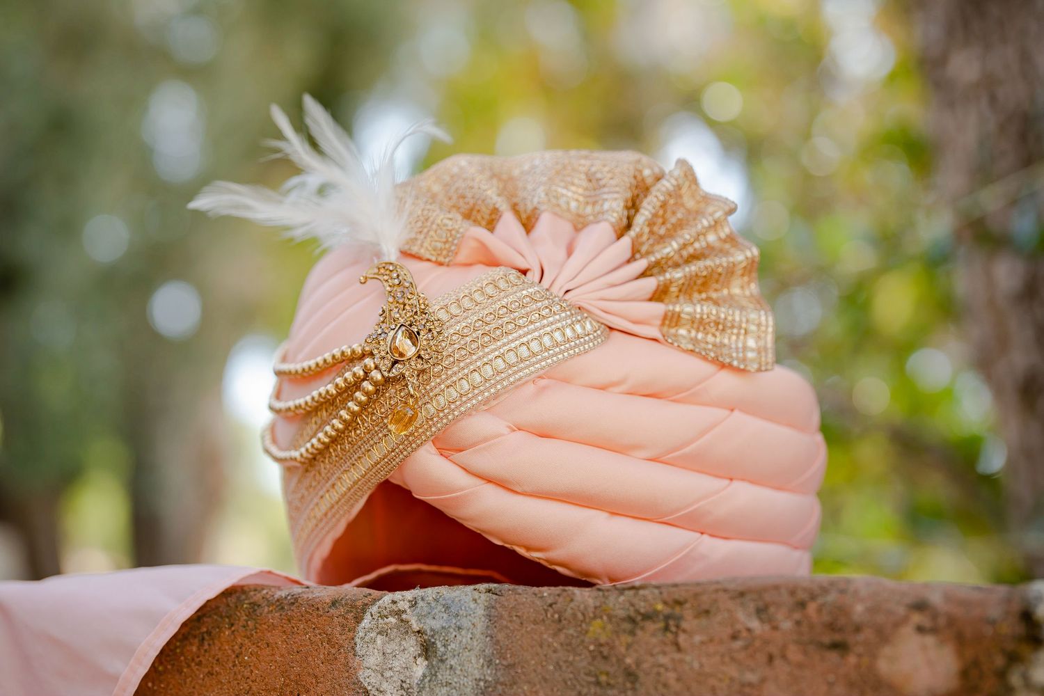 A delicate peach-colored macaroon decorated with gold details sits on a textured surface with bokeh background.