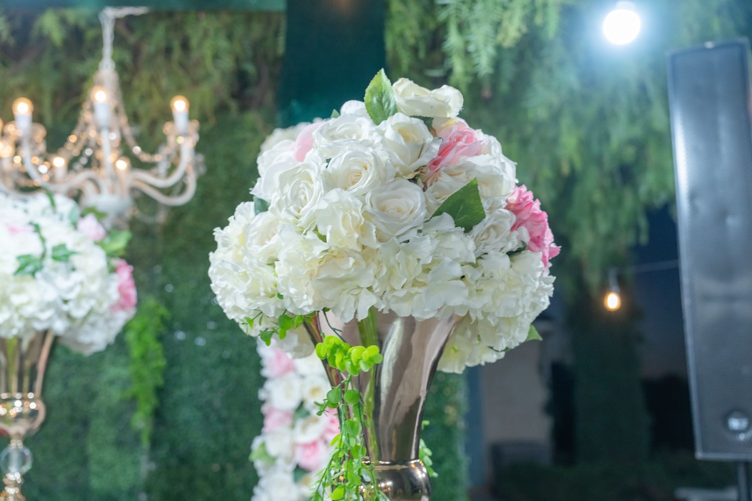 Elegant outdoor wedding reception setup with white hydrangea centerpieces and crystal chandeliers hanging from trees.