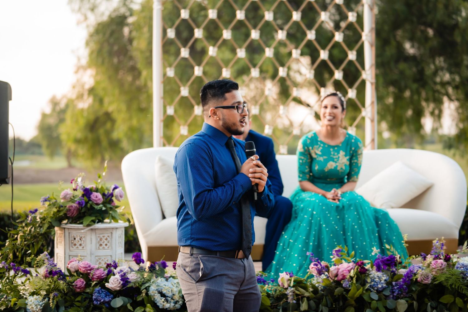 Couple in blue and teal outfits share intimate moments during outdoor photo session with floral arrangements.