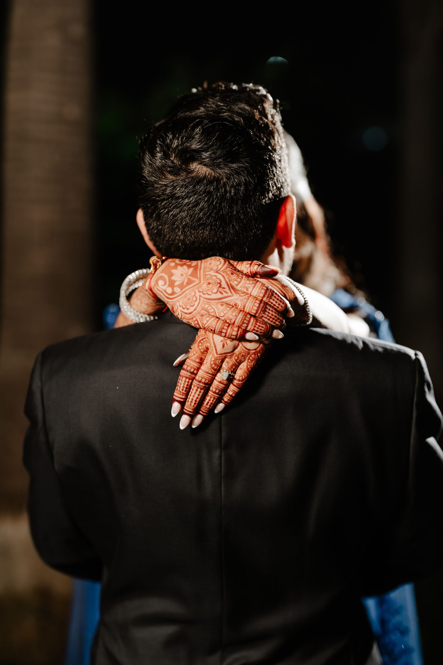 Close-up of henna decorated hands resting on formal black suit jacket.