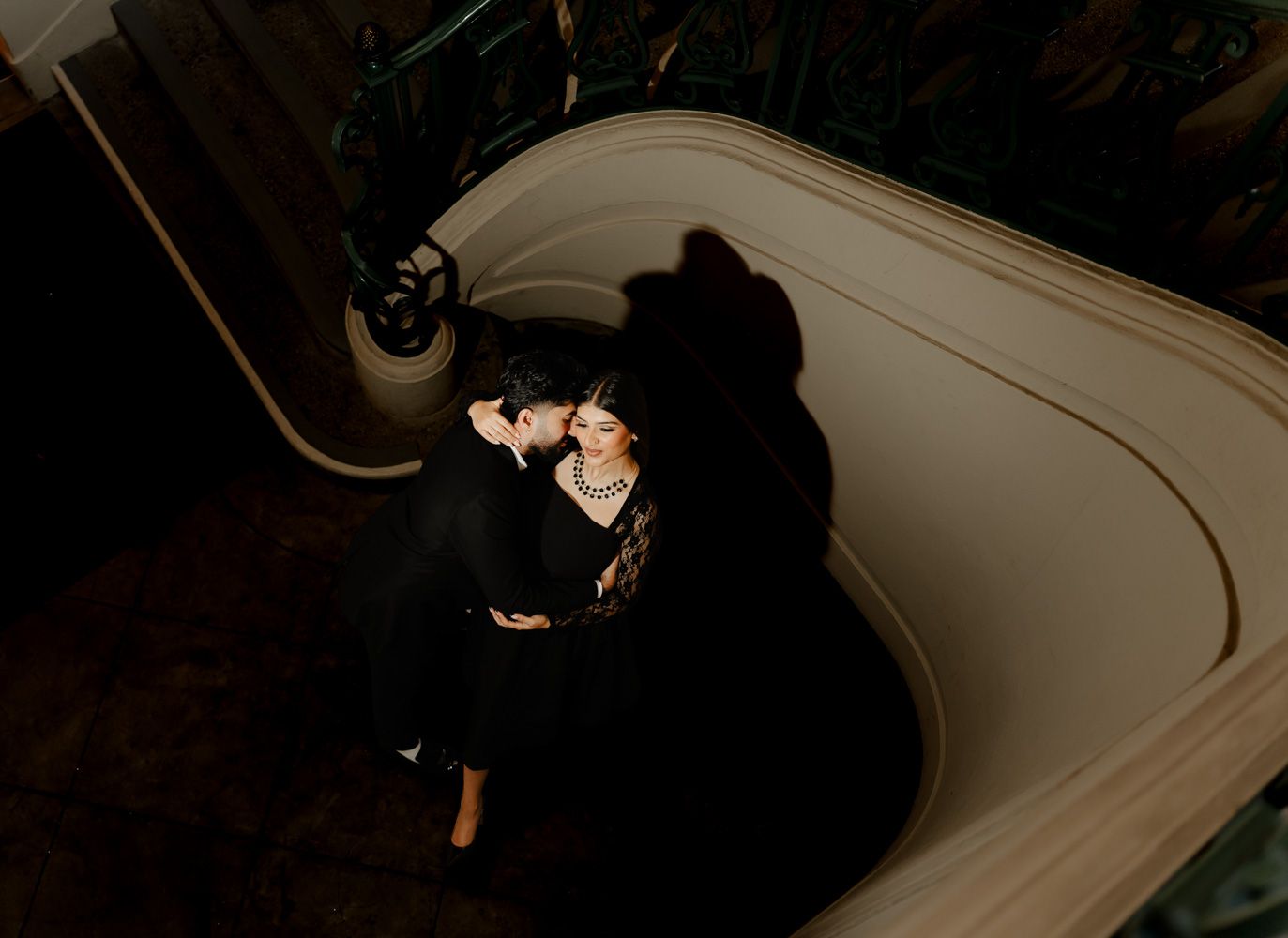 Aerial view of a couple embracing on a curved staircase, captured in dramatic lighting.