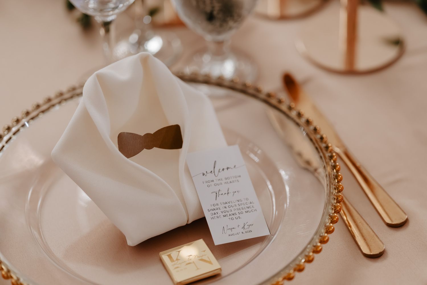 Wedding place setting with gold cutlery and beaded charger plate in neutral tones.