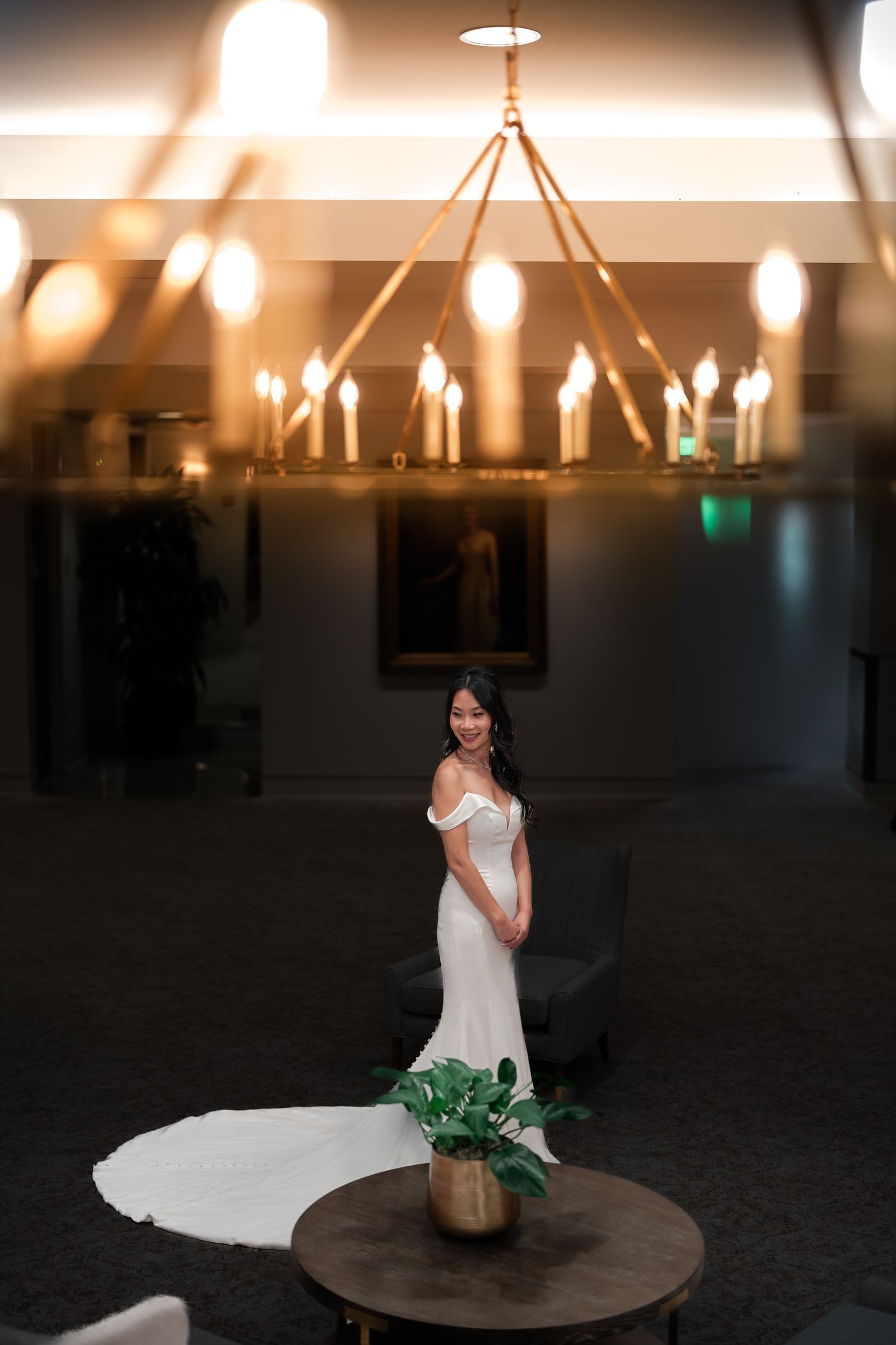 A bride in a white wedding dress poses on a round table under elegant pendant lighting.