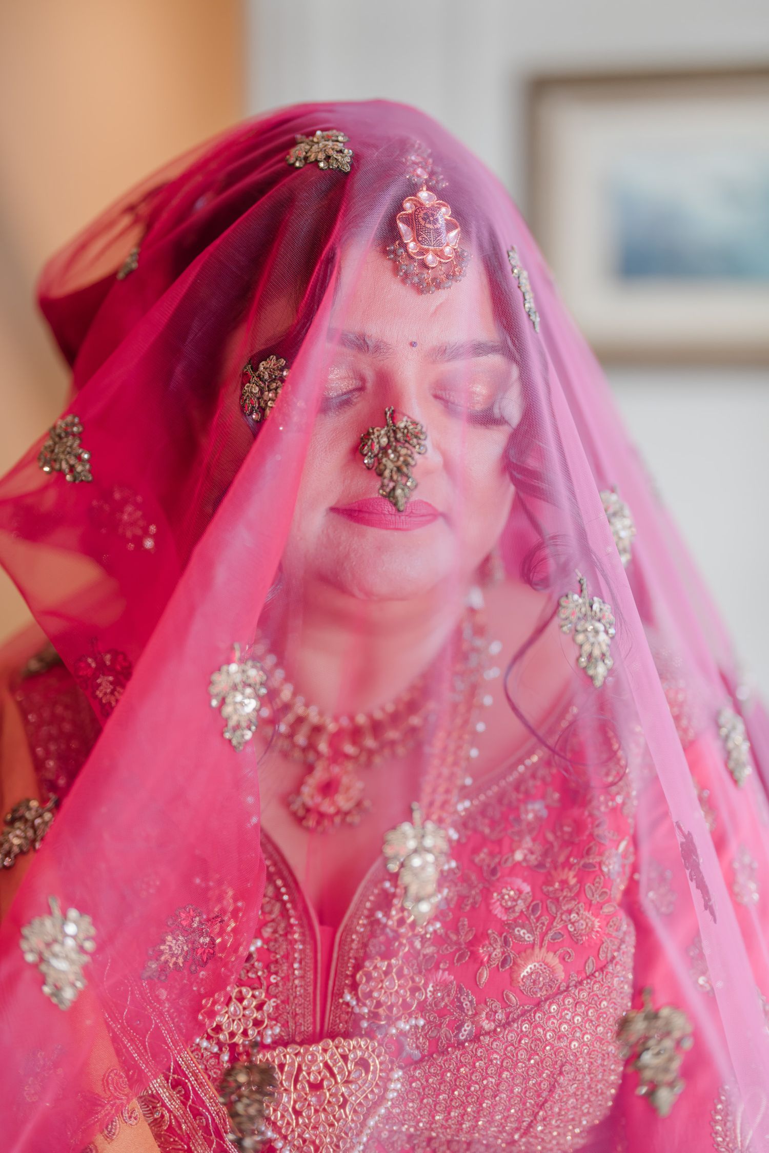 A bride wearing a vibrant pink embroidered veil and traditional Indian wedding attire with intricate beadwork details.