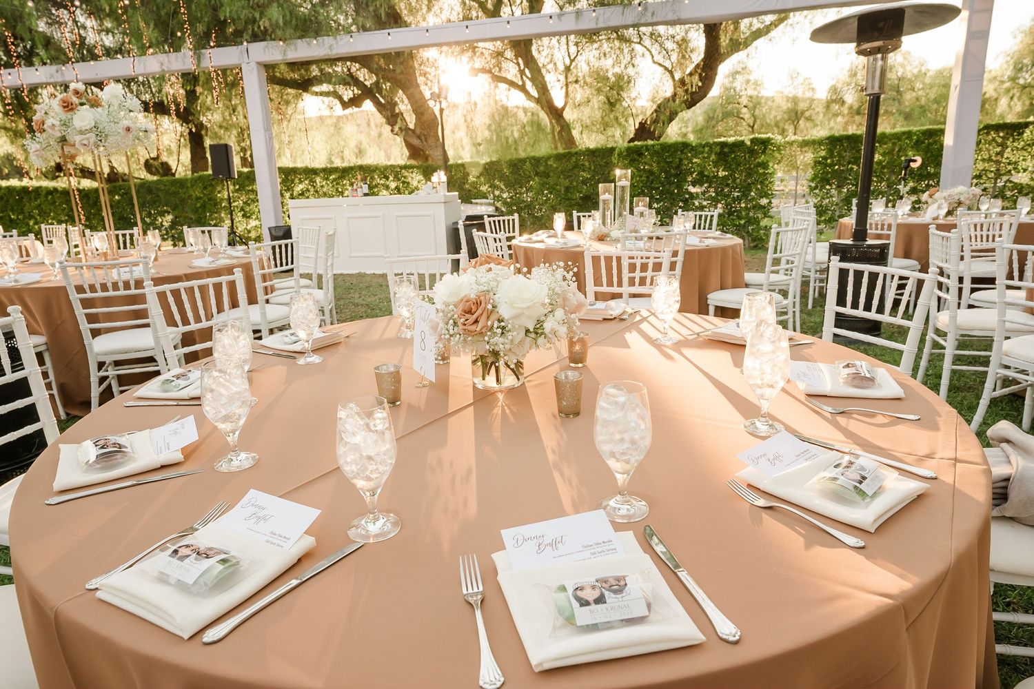 Elegant outdoor wedding reception setup with round tables and white chairs under natural sunlight.