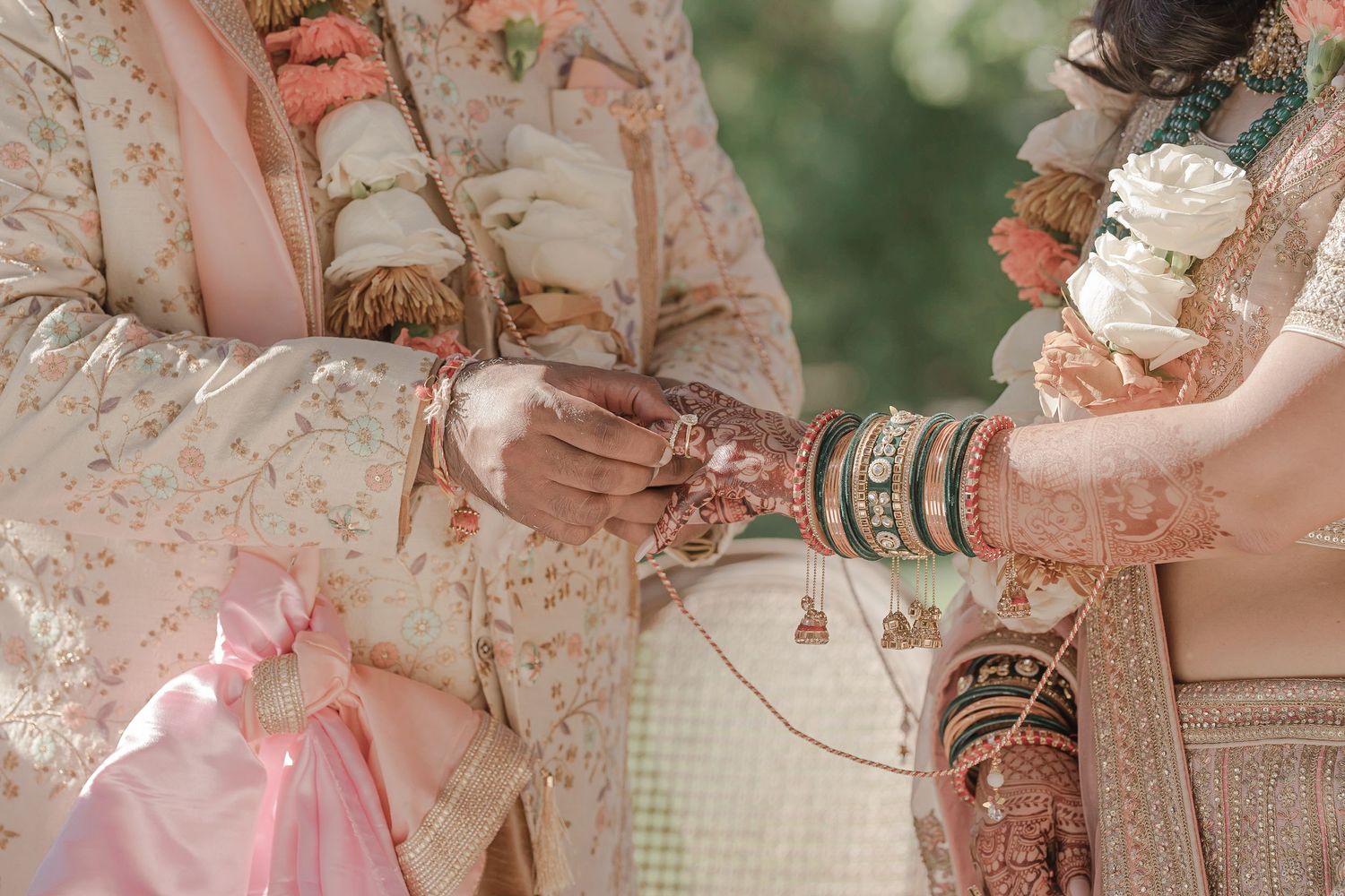 A couple in traditional Indian wedding attire holds hands during a ceremony, adorned with henna and bangles.