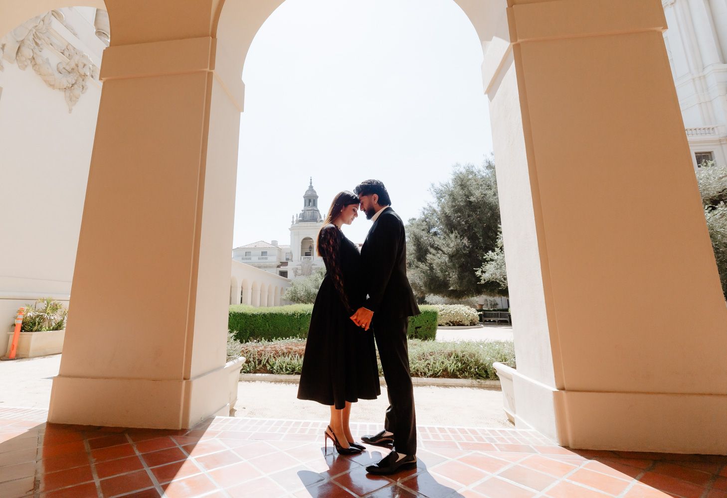 Romantic couple sharing an intimate moment under white arched columns of an elegant building.