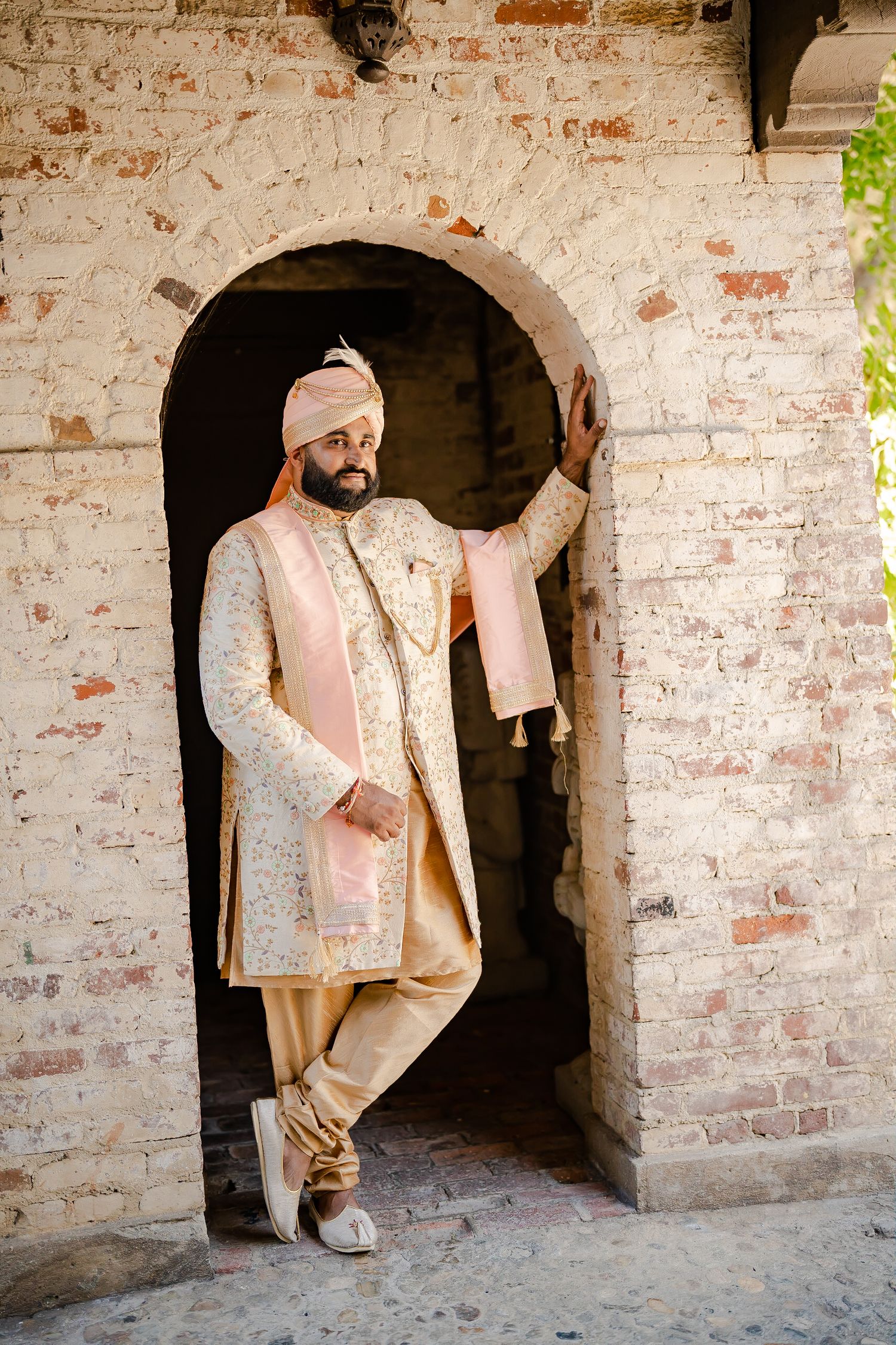 Traditional Indian groom poses in ornate cream sherwani against rustic brick archway in artistic photo sequence.
