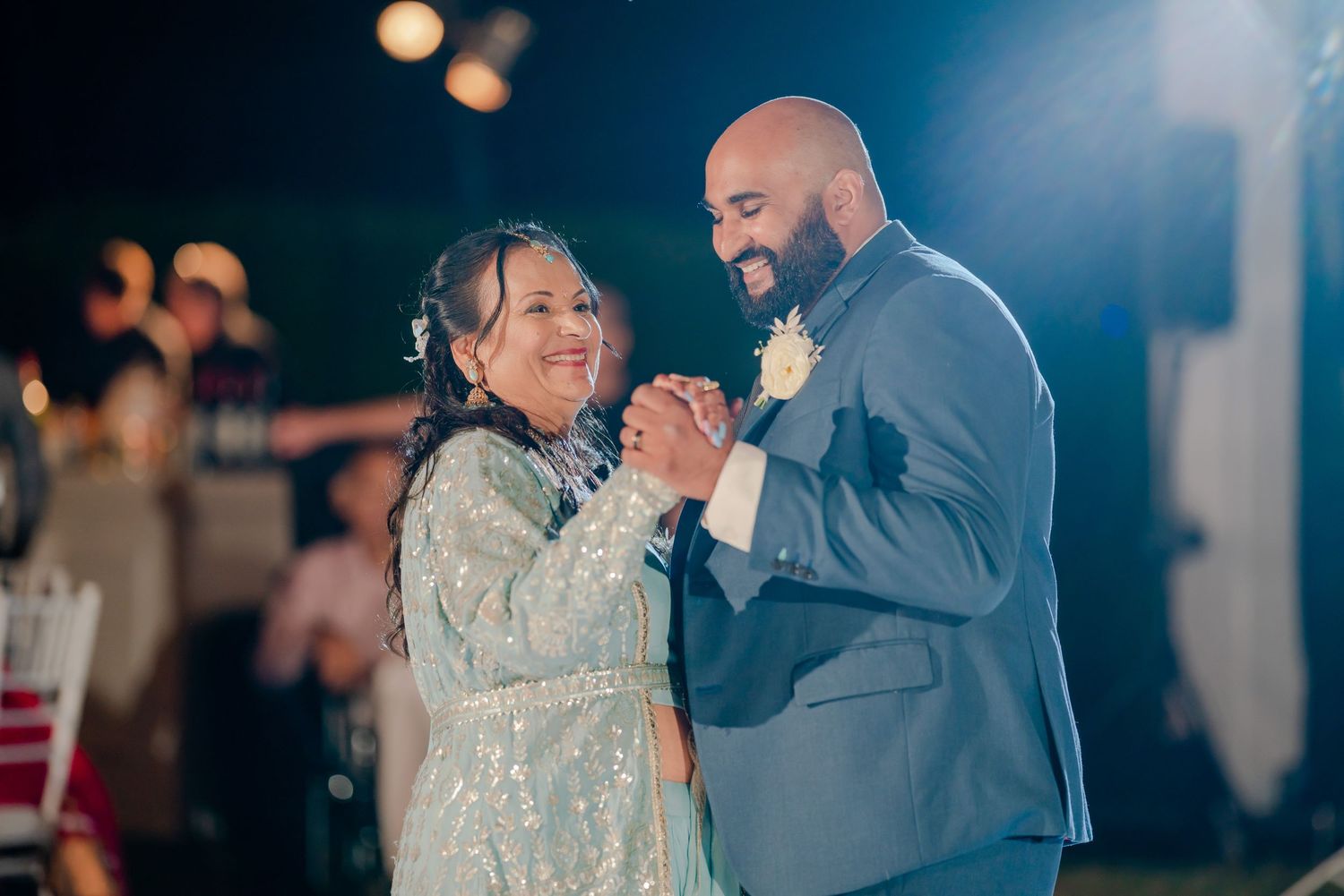 A couple dances together at a wedding reception with romantic lighting and sparkles in the background.