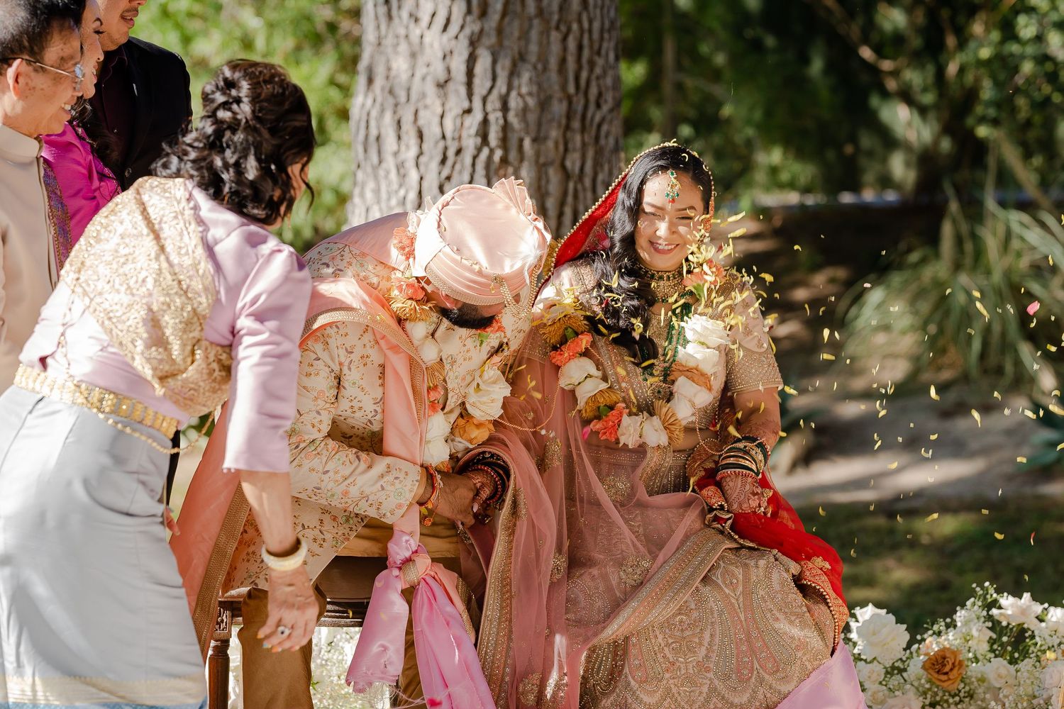 Wedding party members in peach and coral outfits pose together in a garden setting.