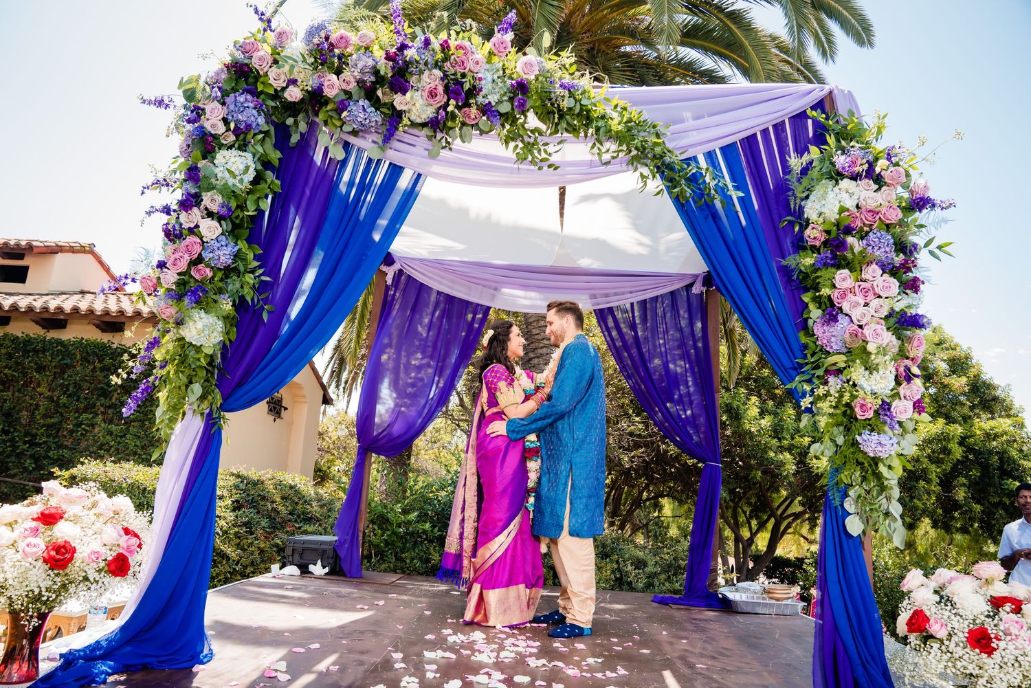 Colorful Indian wedding decor with vibrant blue drapes and pink floral arrangements adorning an outdoor ceremony space.