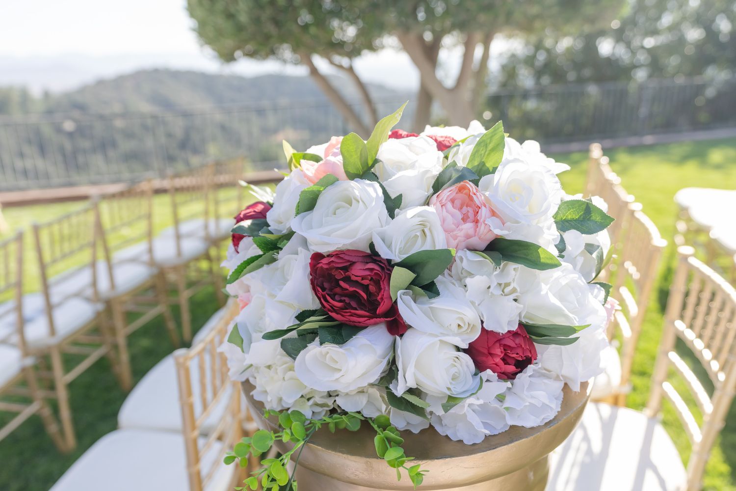 Elegant floral centerpieces featuring white and burgundy roses arranged in gold vases for a wedding reception.