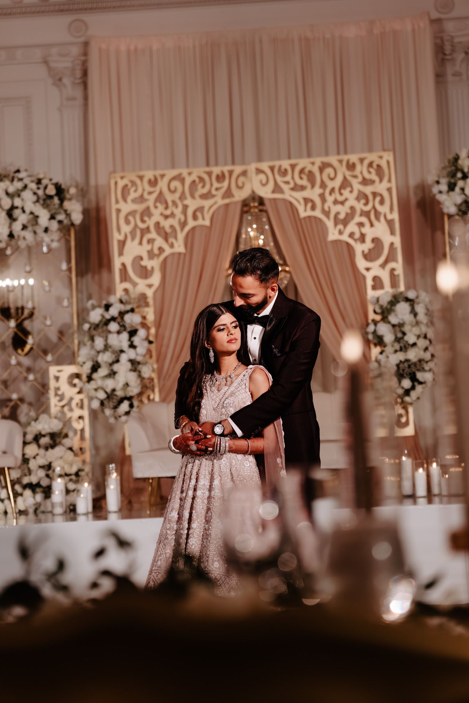 Elegant wedding reception venue with ornate white backdrops and floral arrangements in warm ambient lighting.