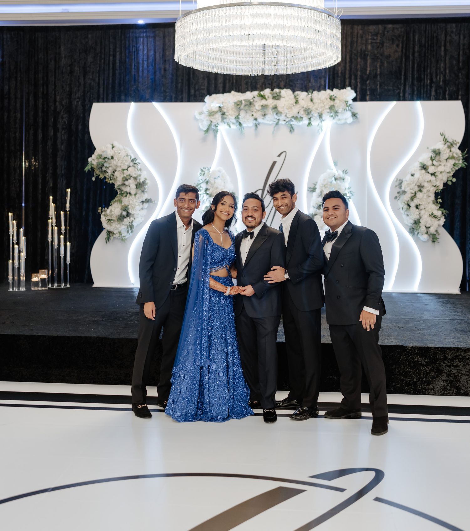 Wedding reception hall with modern white decor, illuminated backdrop and formal guest seating.