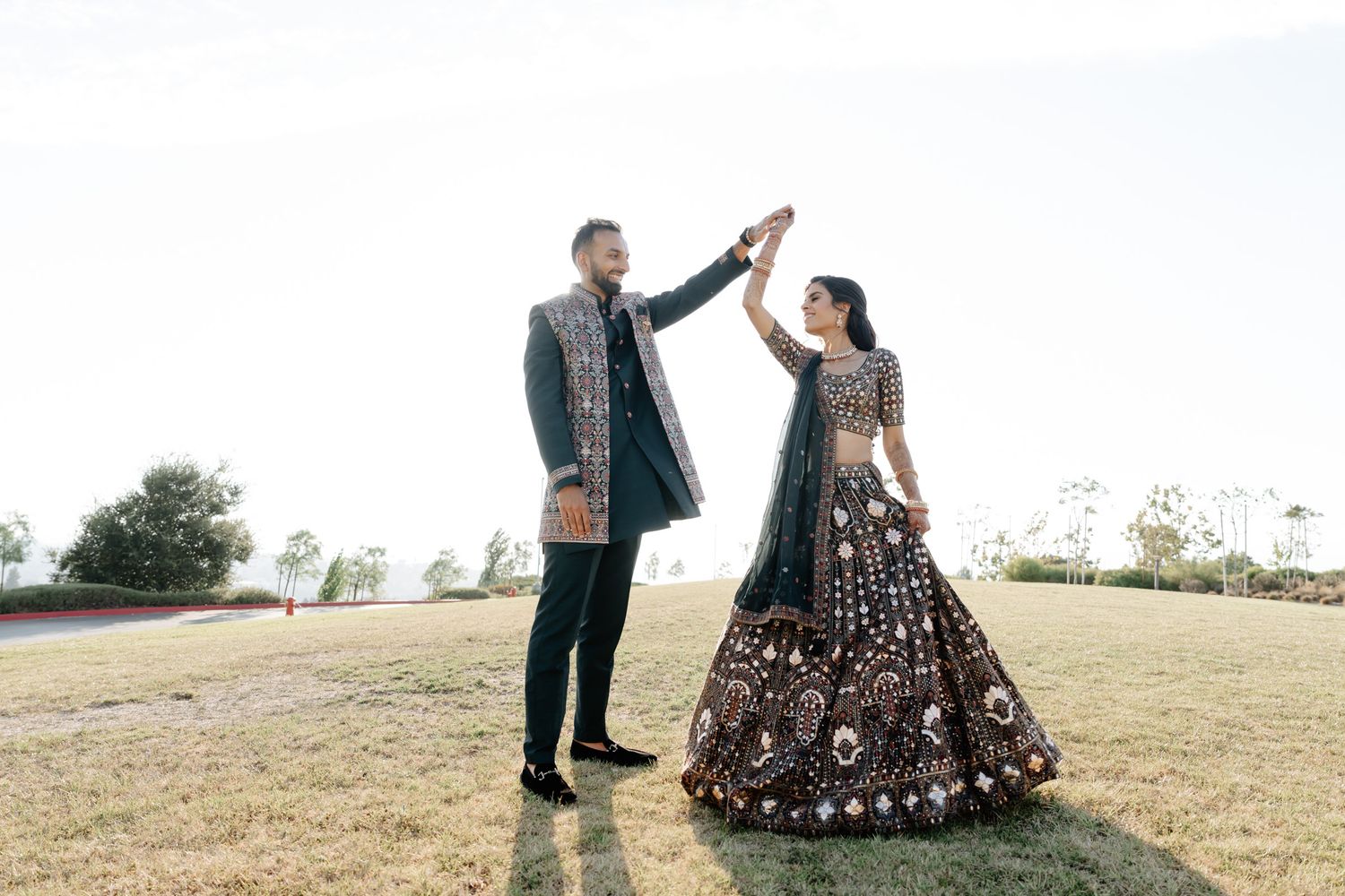 Couple in traditional Indian wedding attire dancing together in an outdoor field.