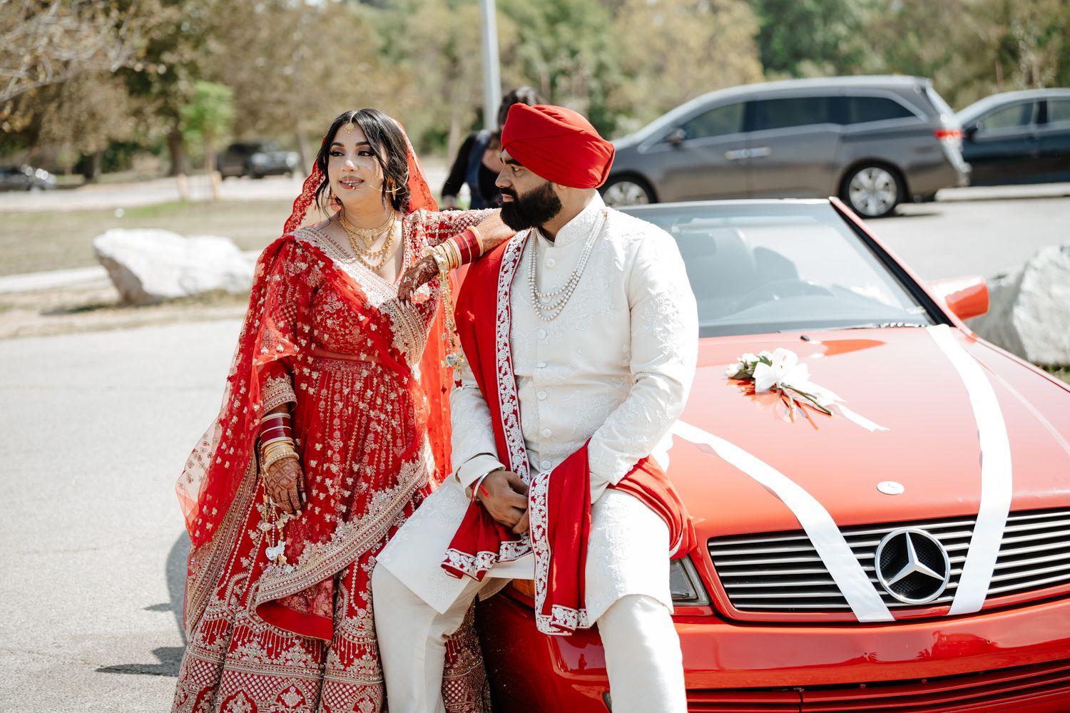 A red and gold embellished bridal lehenga and Mercedes car captured in an outdoor wedding photoshoot.