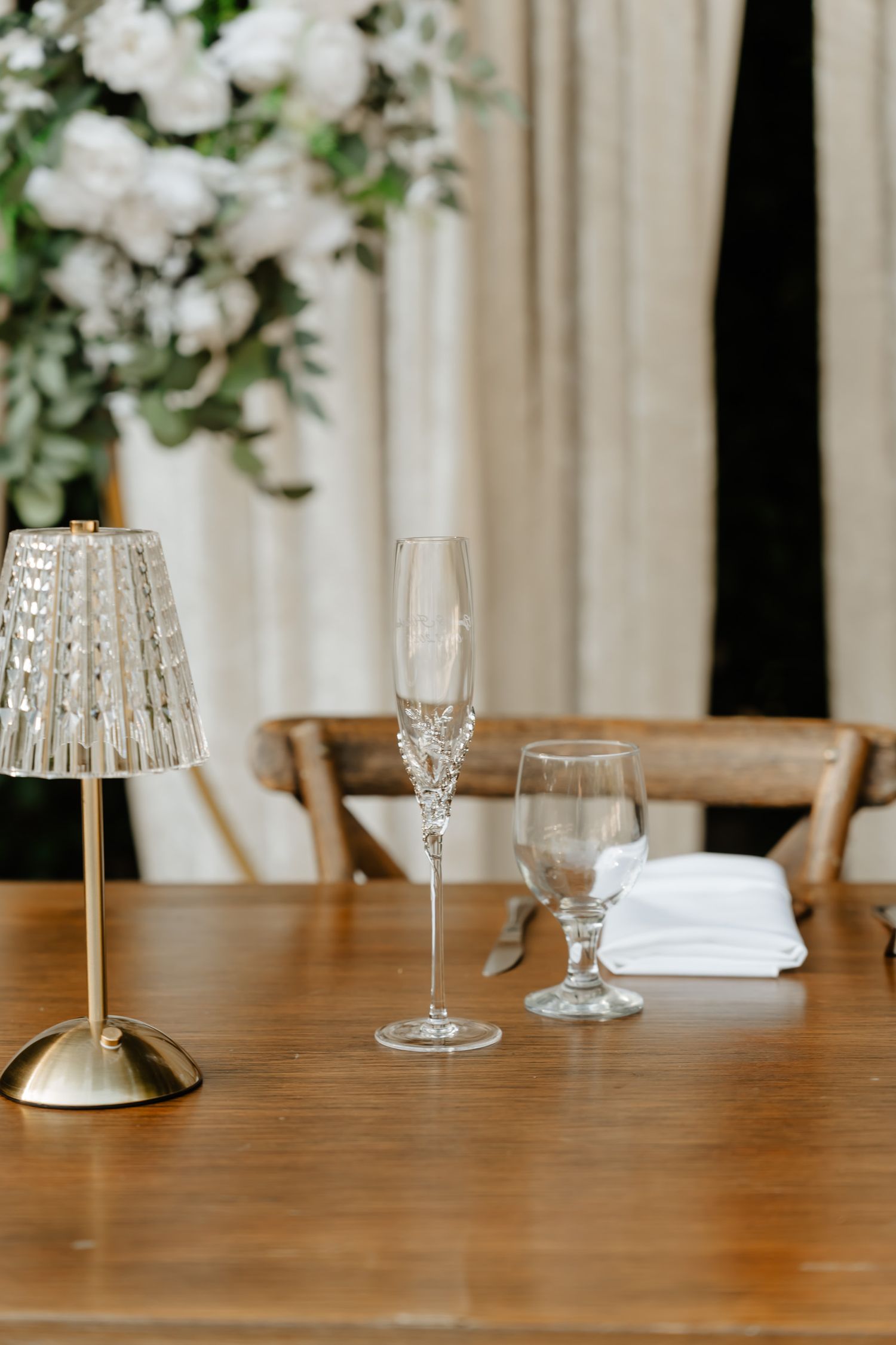 Elegant table setting with crystal glasses, lamp and white floral decor.