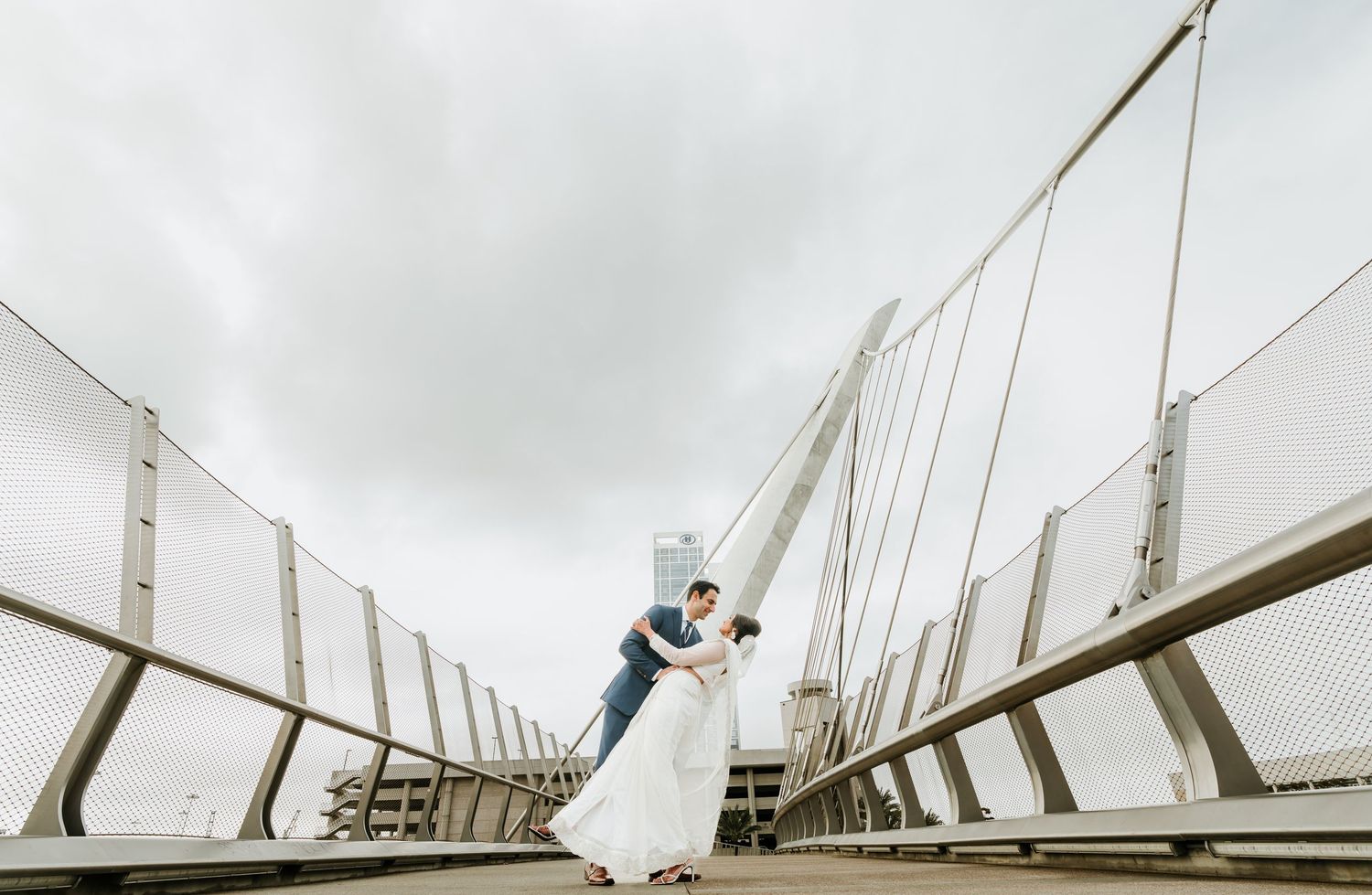 A modern architectural bridge with white geometric arches spans across a cloudy sky in Valencia, Spain.