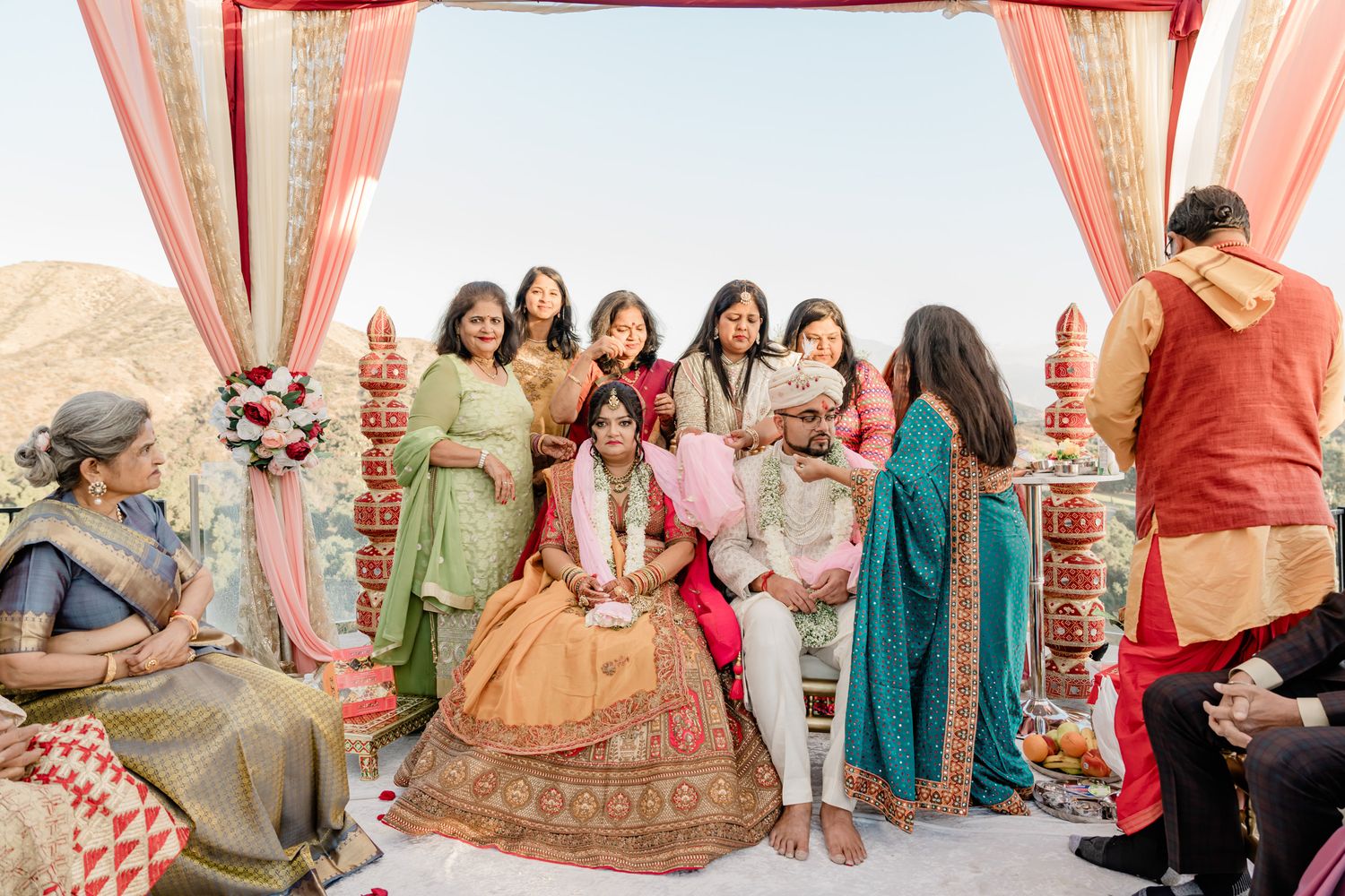 A colorful Indian wedding ceremony with guests in traditional attire gathered under a decorated mandap by the ocean.