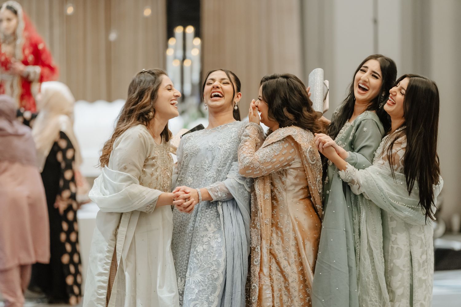 A group of bridesmaids in soft gray traditional South Asian outfits share joyful moments at a wedding celebration.