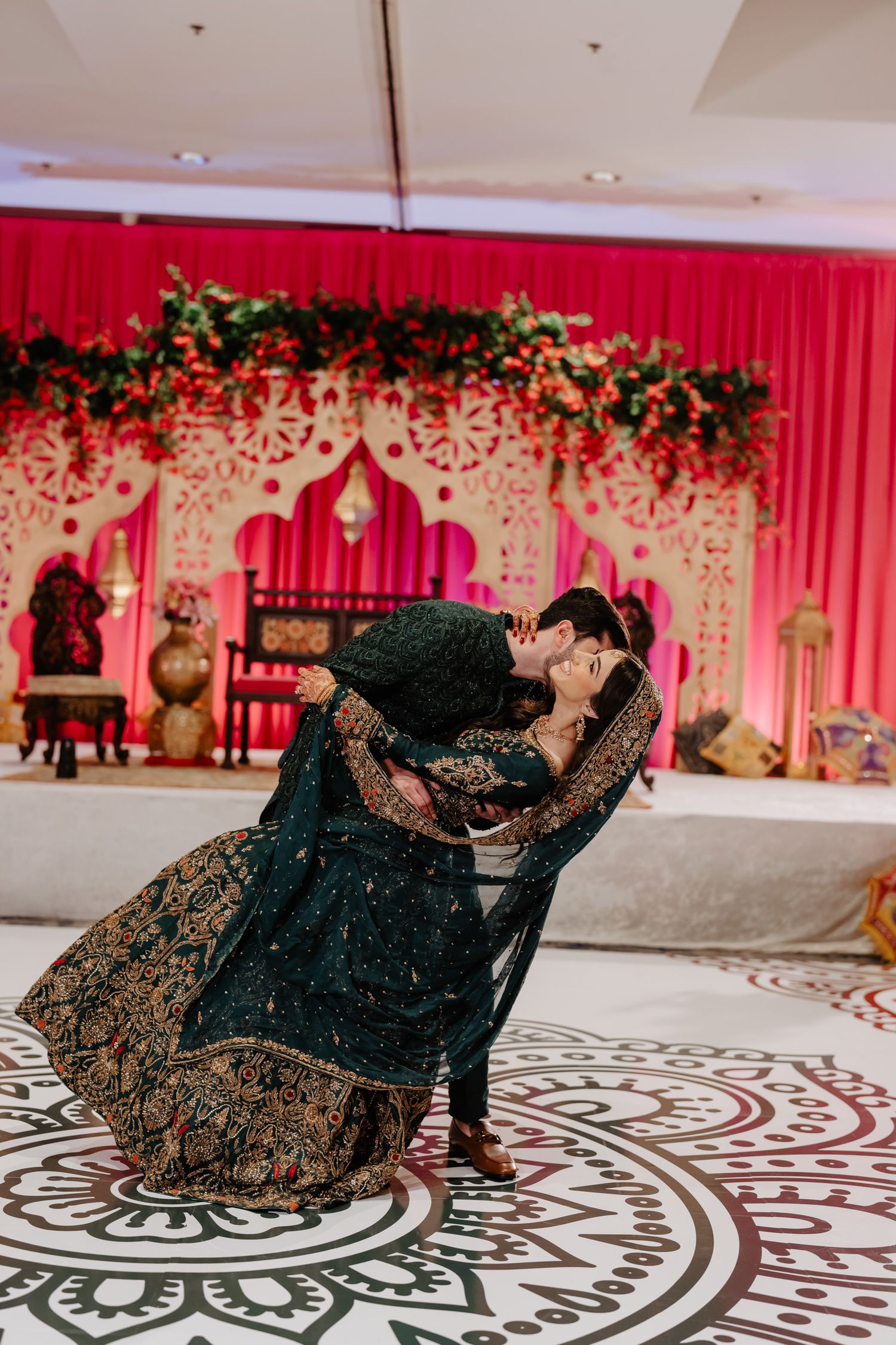 Elegant dark blue and gold embroidered lehenga twirling on a patterned dance floor with pink decor backdrop.
