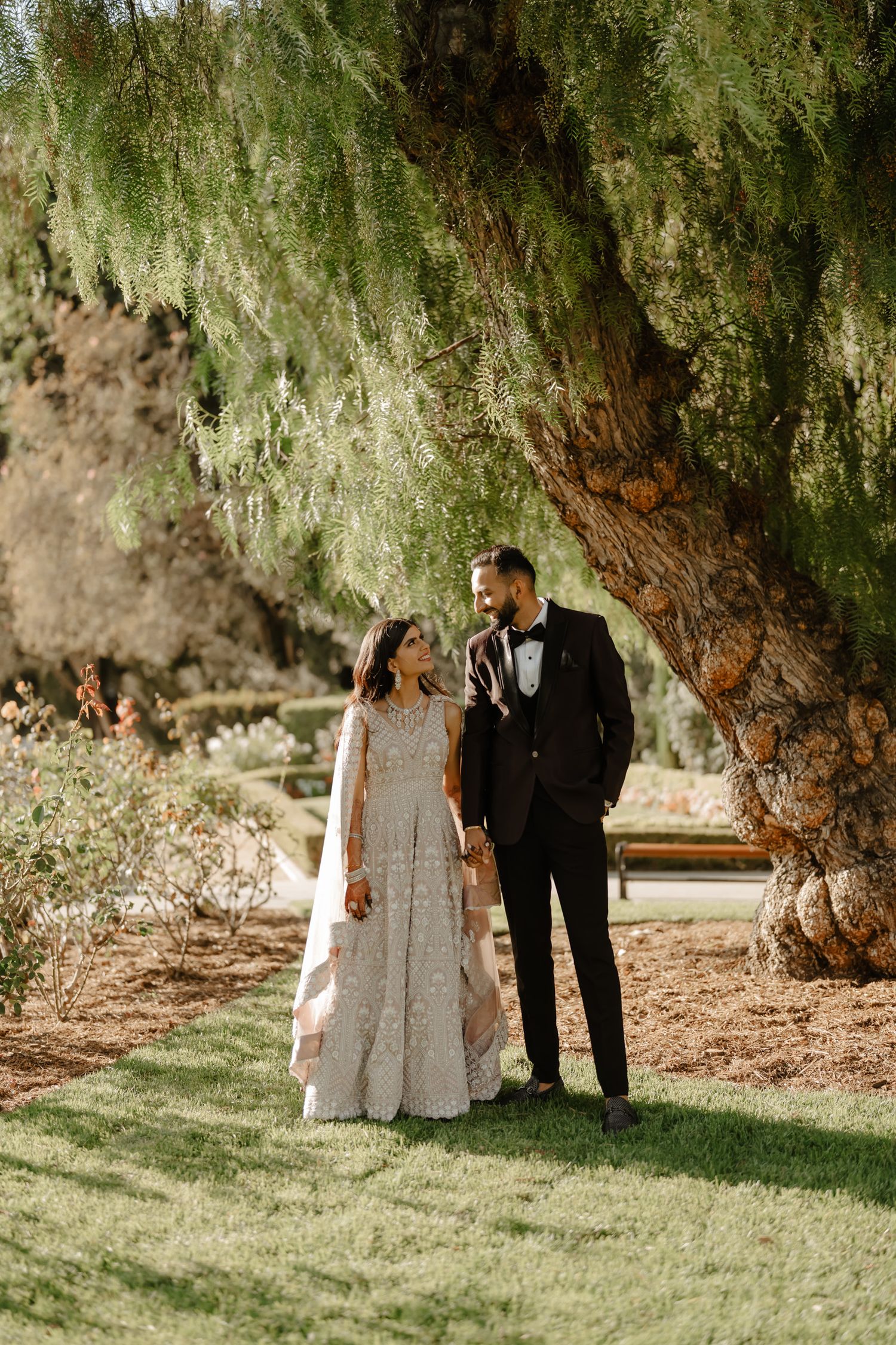 A romantic wedding photoshoot under large willow trees with natural lighting and rustic scenery.