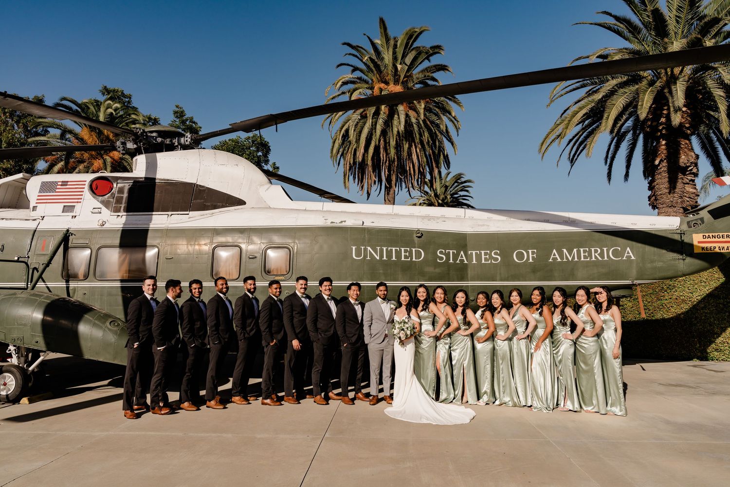 Wedding party group photo taken in front of an aircraft with palm trees in the background.