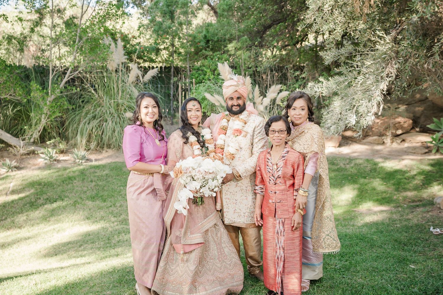 A cheerful group wearing coordinated beige and coral outfits poses together in a lush garden setting.