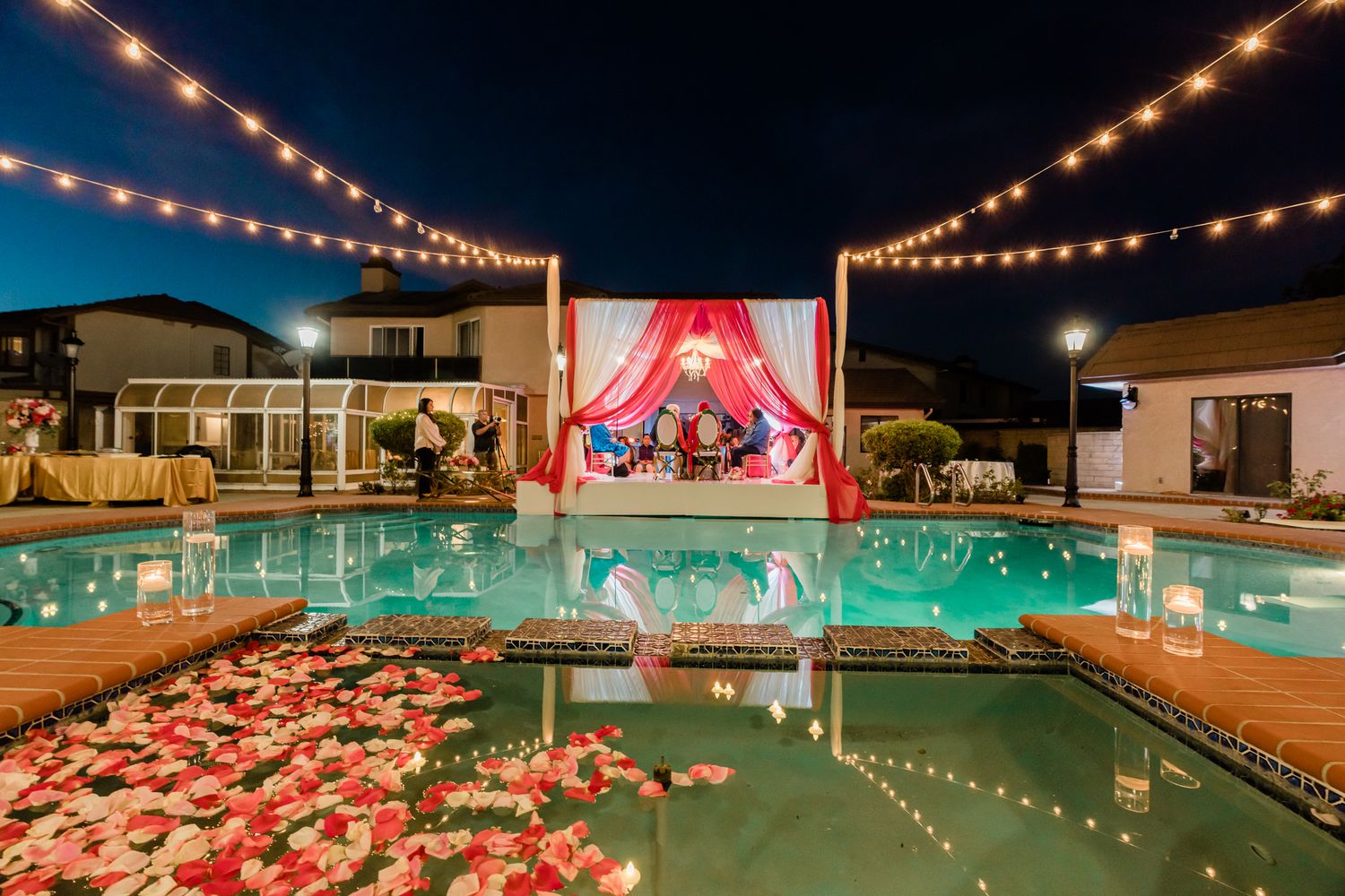 Illuminated outdoor pool area decorated with pink fabric and string lights for an elegant evening event.