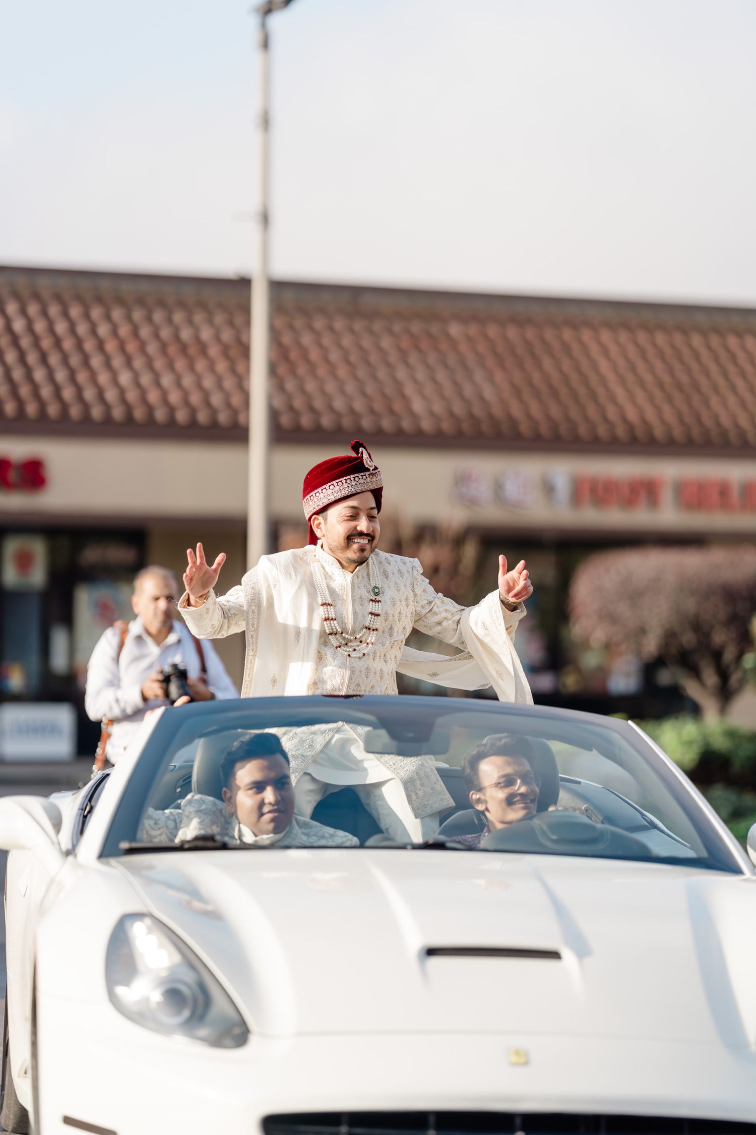 White luxury convertible sports car carrying wedding party members along a street.