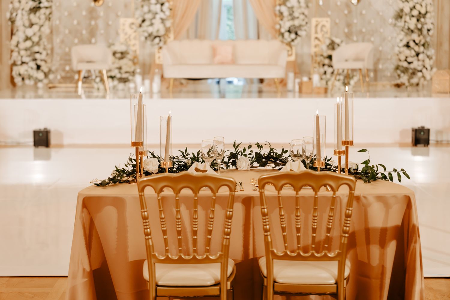 Elegant wedding reception setup with golden chairs and floral arrangements in a light-filled banquet hall.