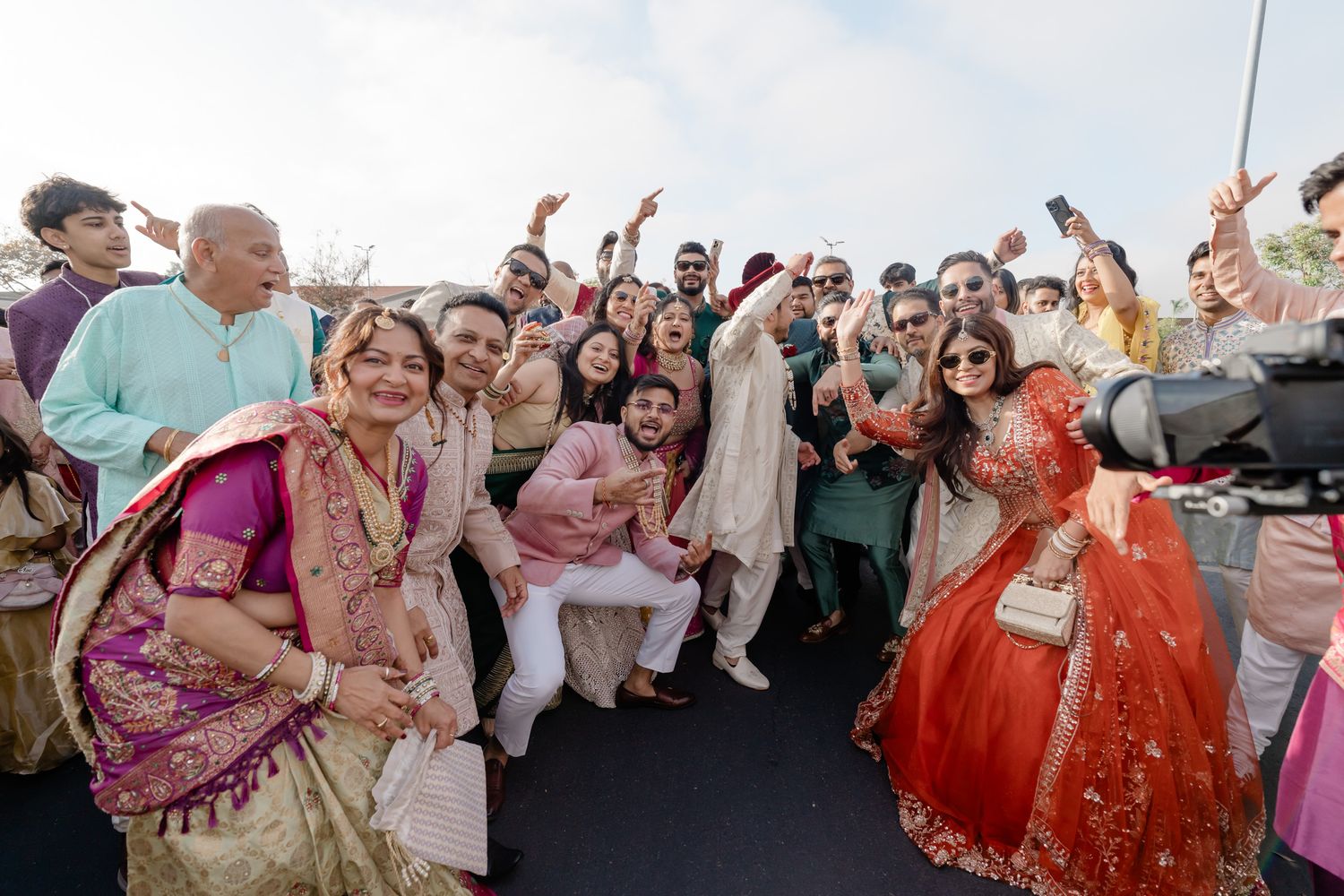Joyous crowd celebrating at an outdoor Indian wedding with guests dancing and cheering.