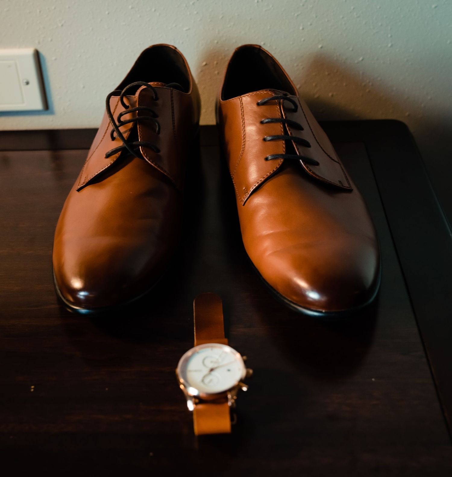 A pair of brown leather dress shoes with laces sits elegantly on a dark wooden surface.