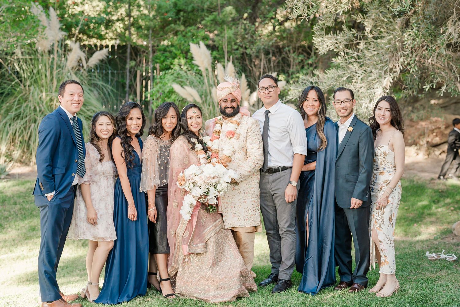 Wedding party poses together outdoors wearing coordinated outfits in blue, pink and neutral colors.