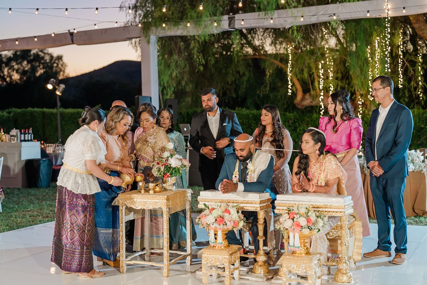 Evening wedding reception with guests gathering around tables under illuminated string lights.
