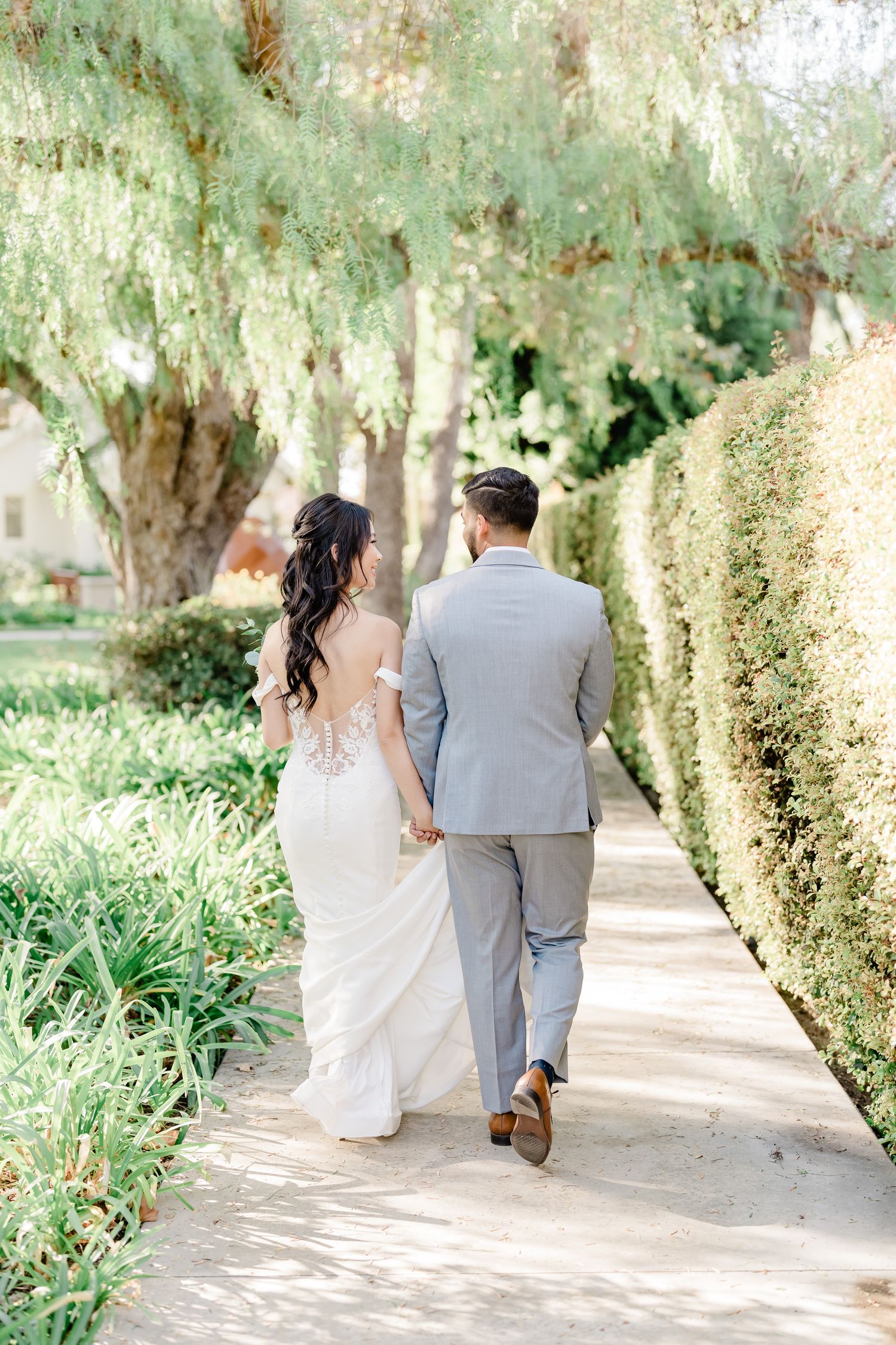Couple walking along a garden pathway holding hands on their wedding day, captured in a romantic sequence.