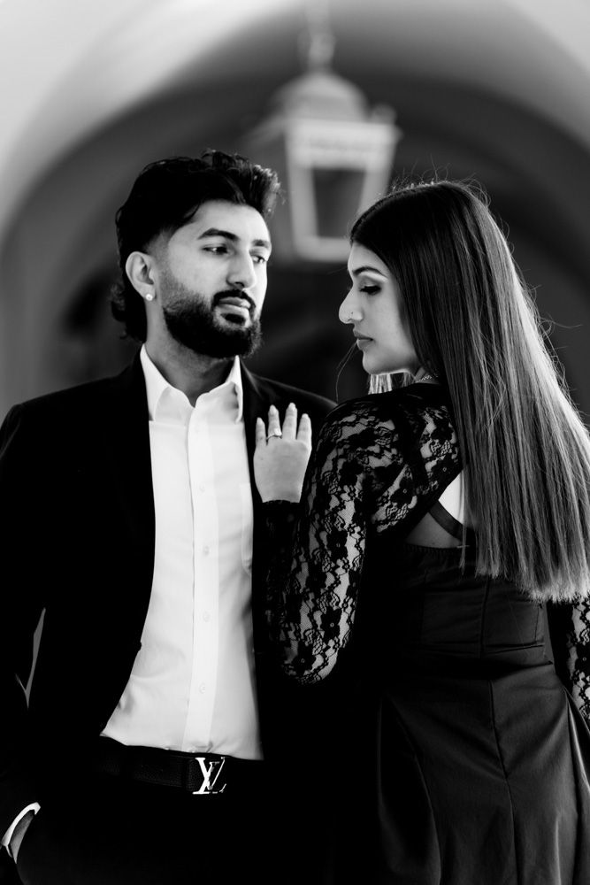 Elegant couple in black formal wear posing under arched corridor in B&W.