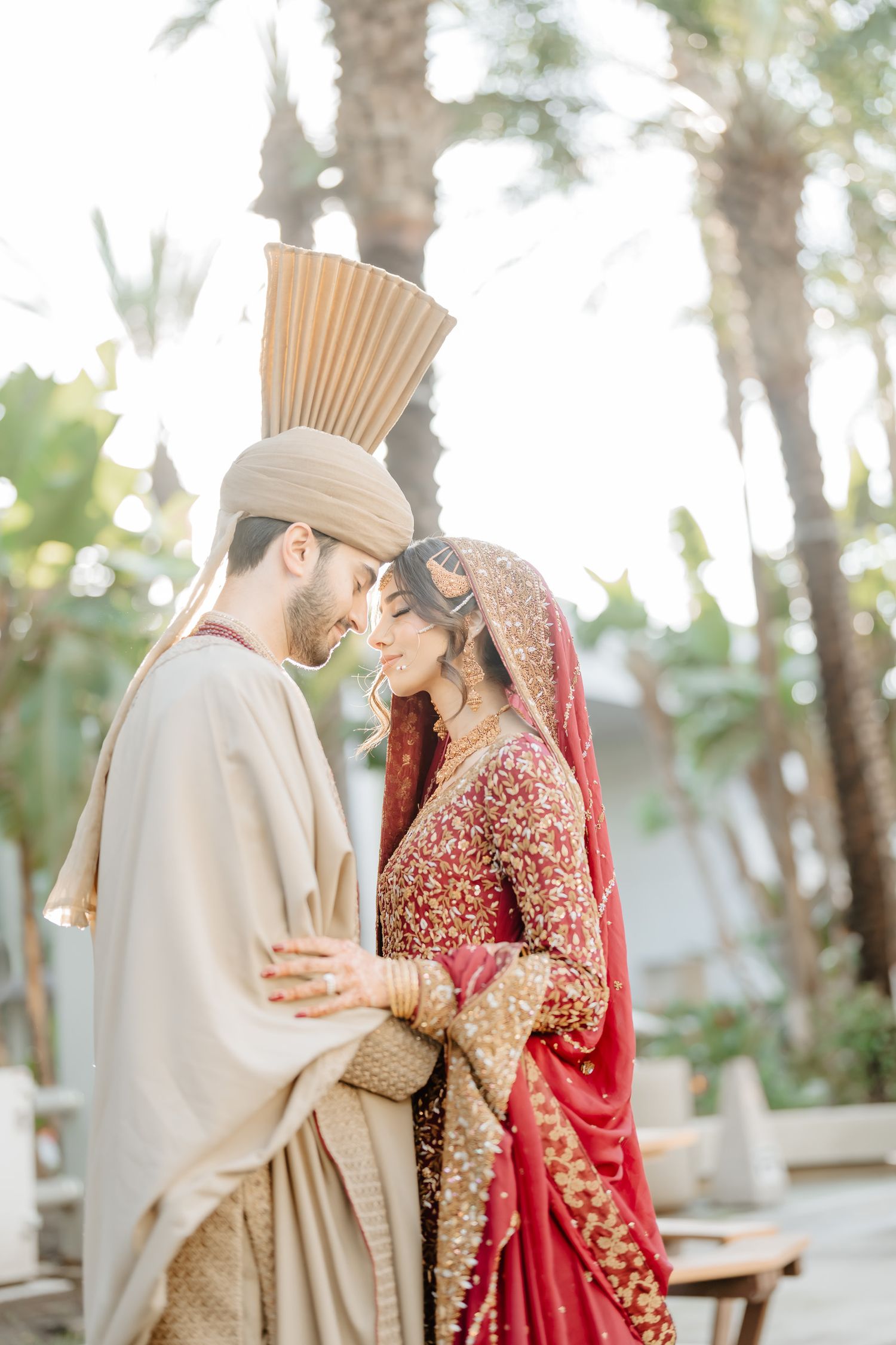 Intimate wedding portrait of couple in traditional South Asian wedding attire surrounded by palm trees.