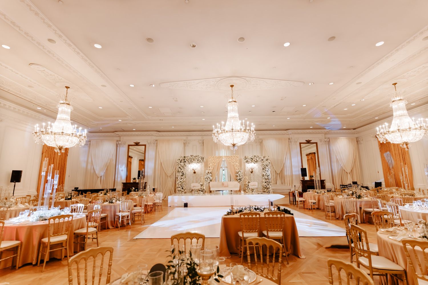 Elegant wedding reception ballroom with crystal chandeliers and round tables set for dining.