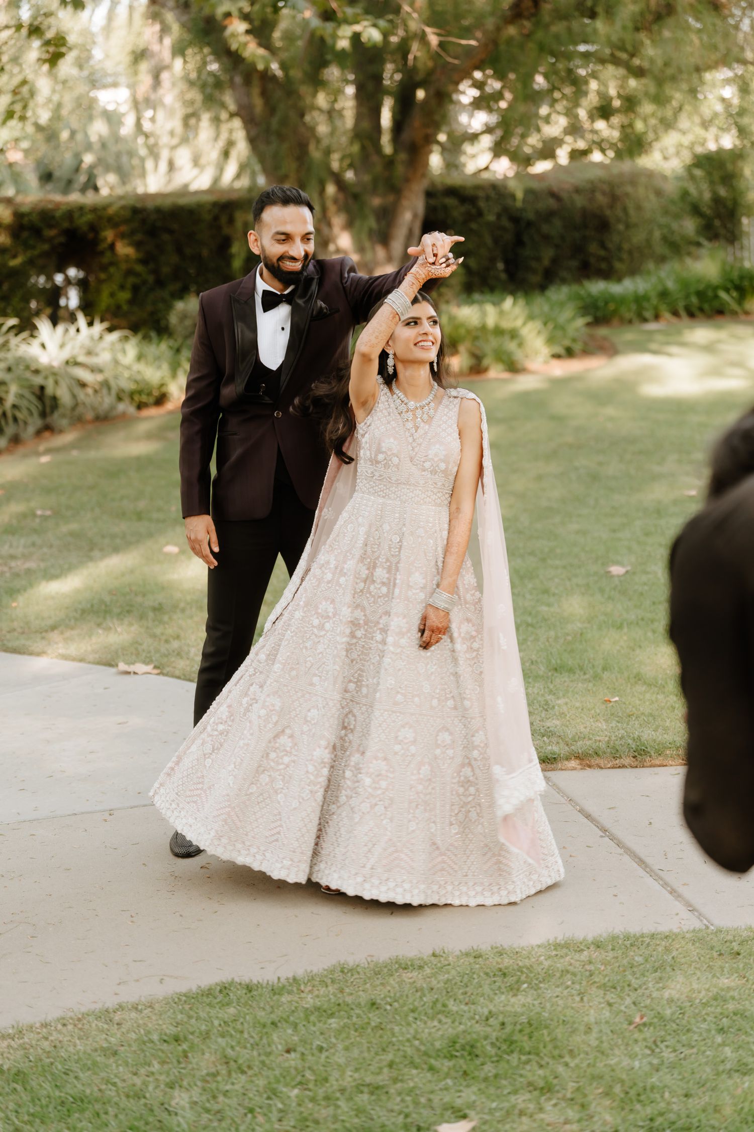 Wedding couple walking together on a garden path with flowing white dress and formal attire.