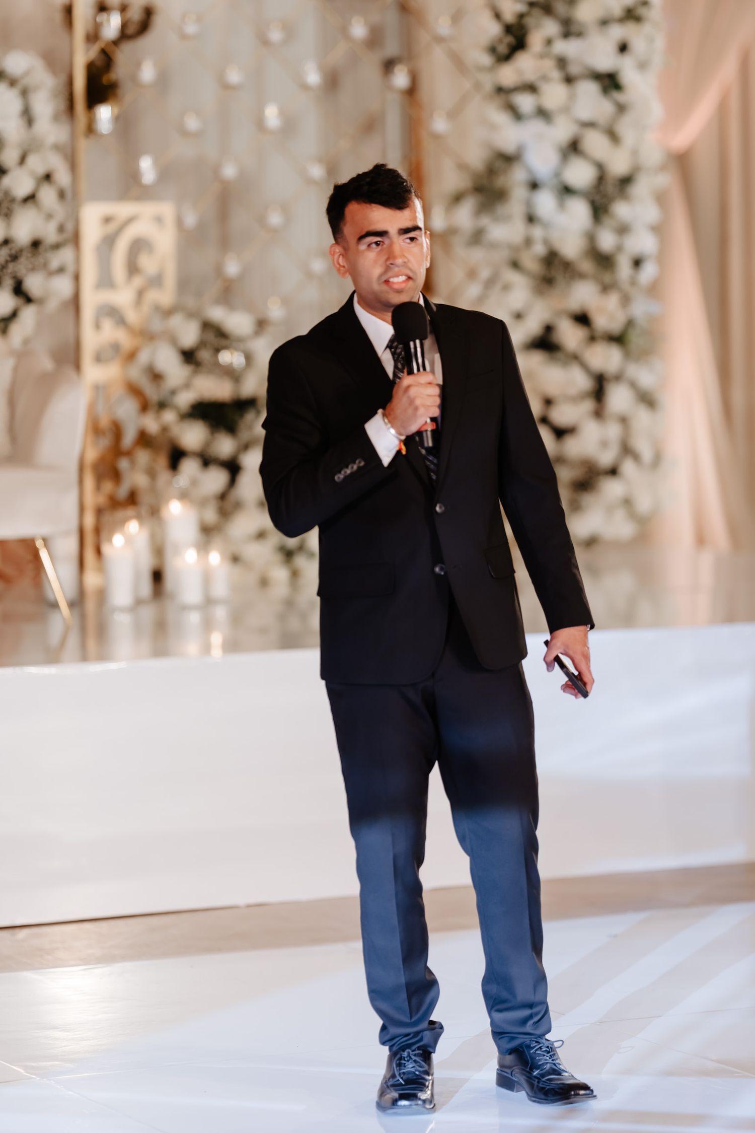 Wedding photographer in a black suit capturing moments at an elegant indoor venue.