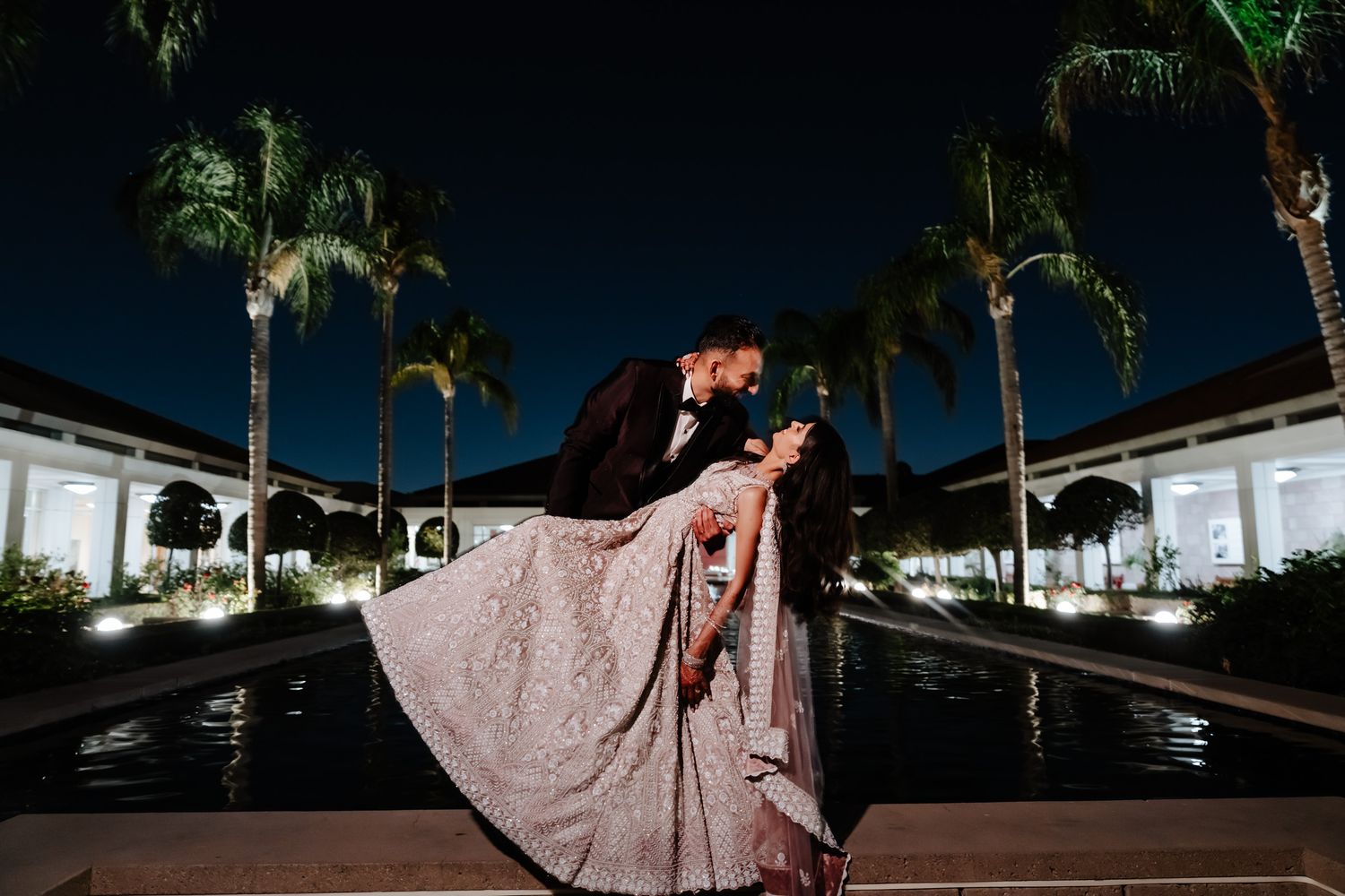 Evening outdoor wedding portraits with palm trees silhouetted against a dramatic night sky.
