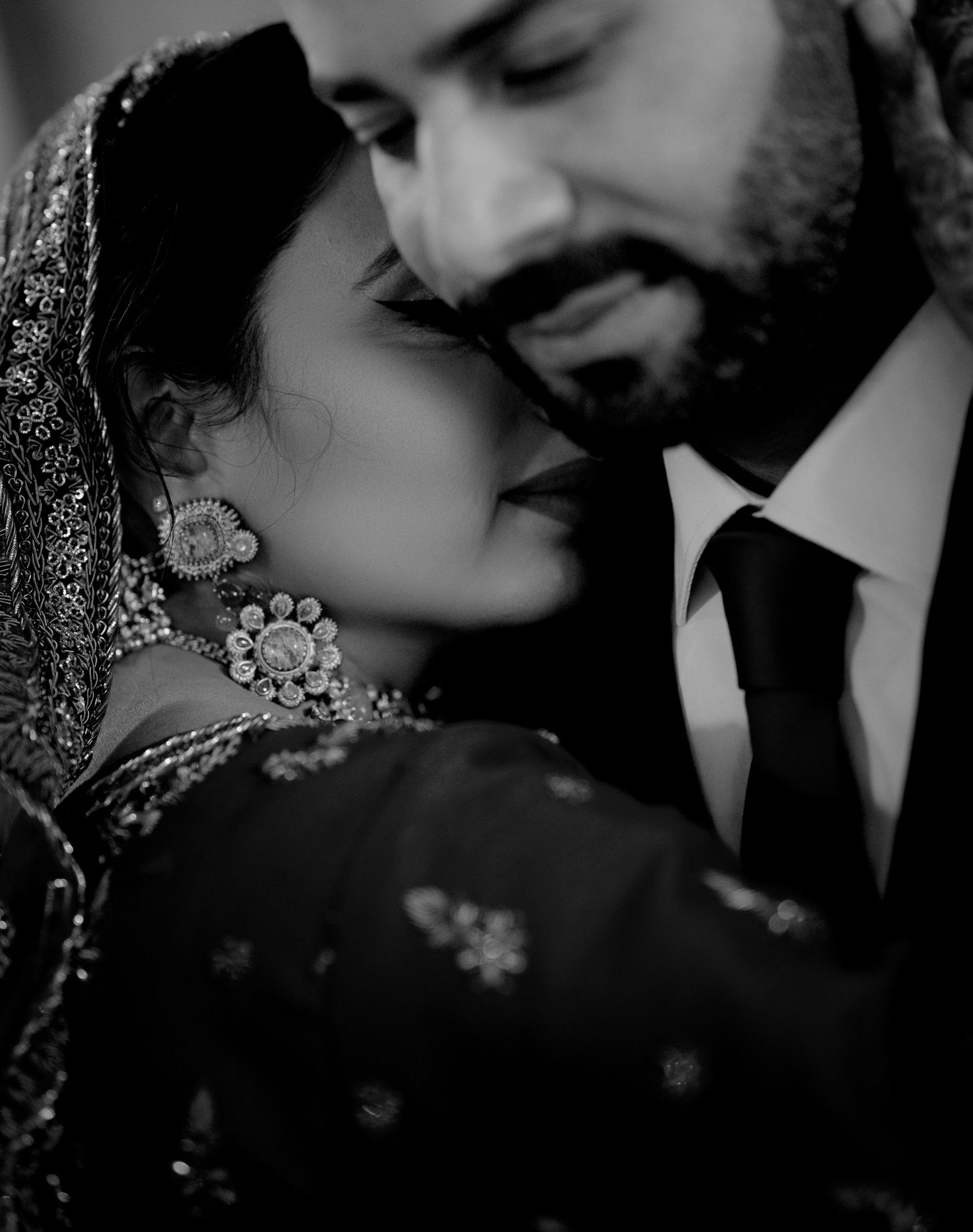A romantic black and white portrait of a couple in traditional South Asian wedding attire sharing an intimate moment.