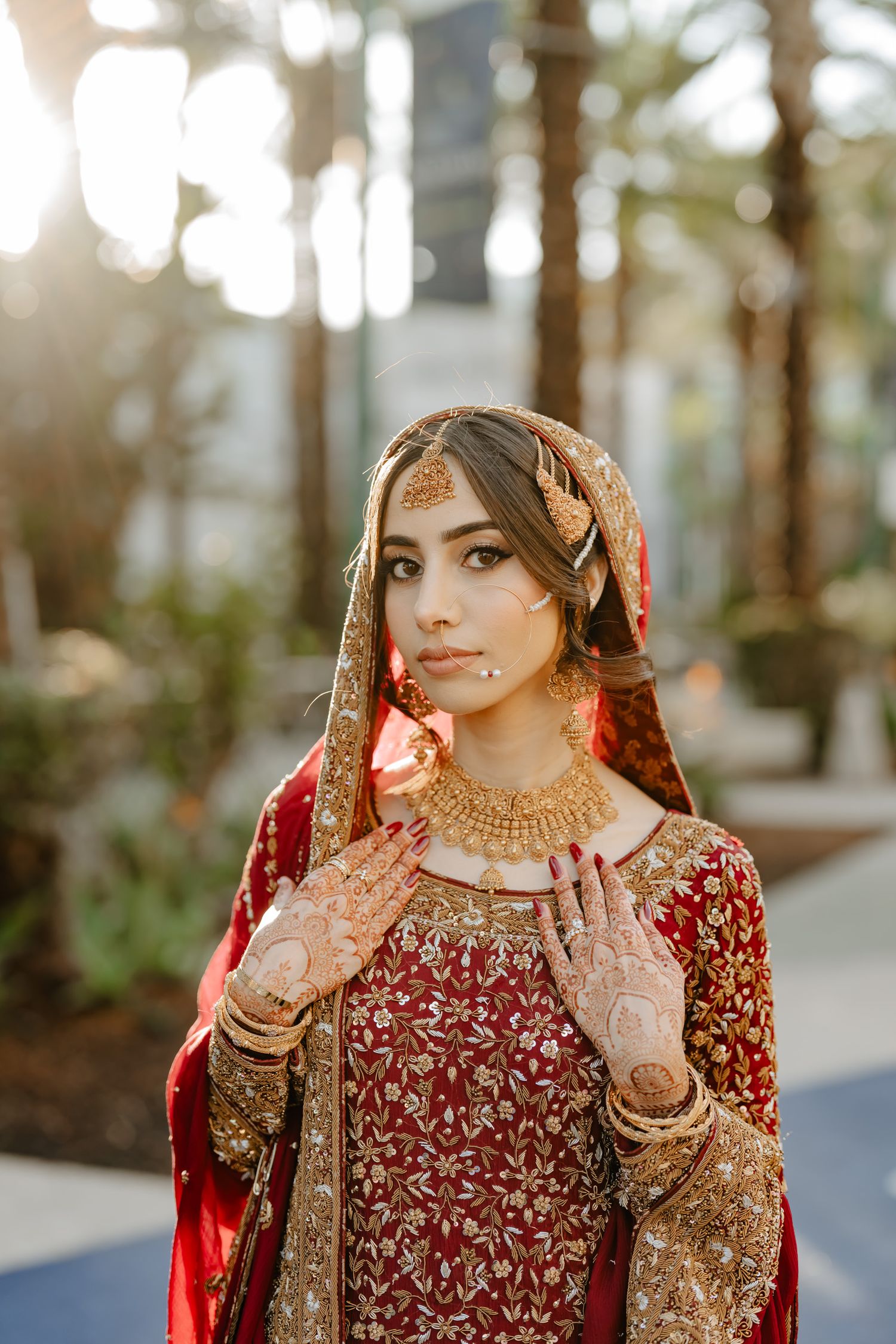 Traditional South Asian bride wearing red and gold attire with intricate henna designs and jewelry.