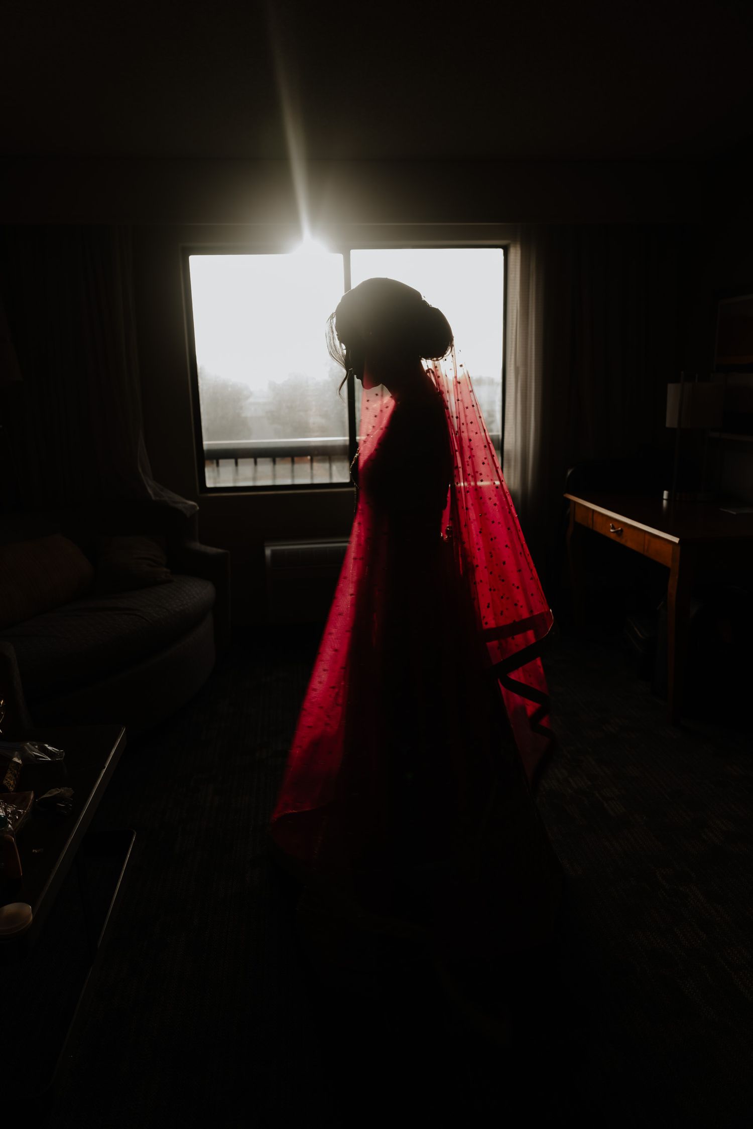 A silhouetted figure in a red sweater stands in front of a bright window in a dark room, creating a dramatic contrast.