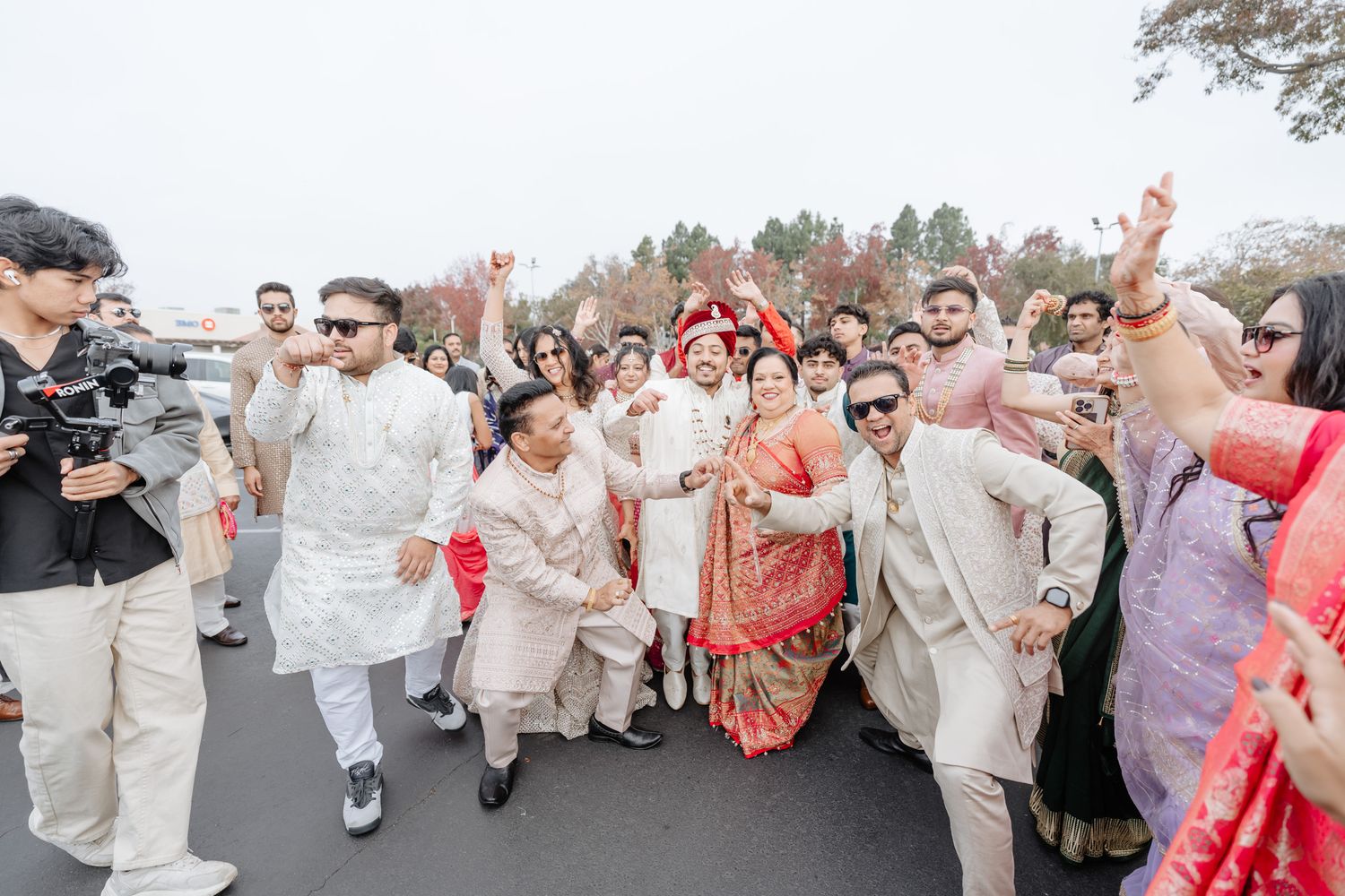 Wedding party jumps and celebrates together on a paved walkway while wearing coordinated beige and coral attire.