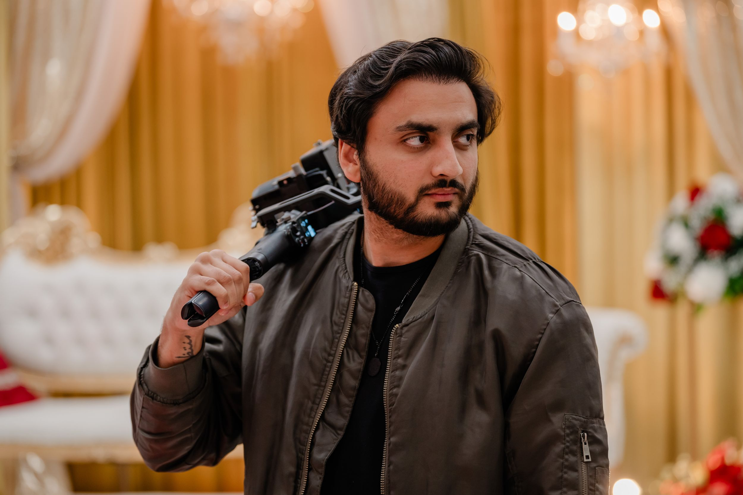Man in brown jacket holding a video camera on his shoulder at an elegant event venue.