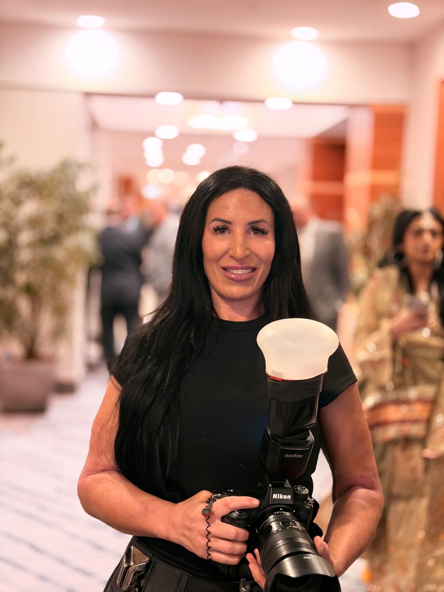 Female photographer smiling with Nikon camera and flash at event.